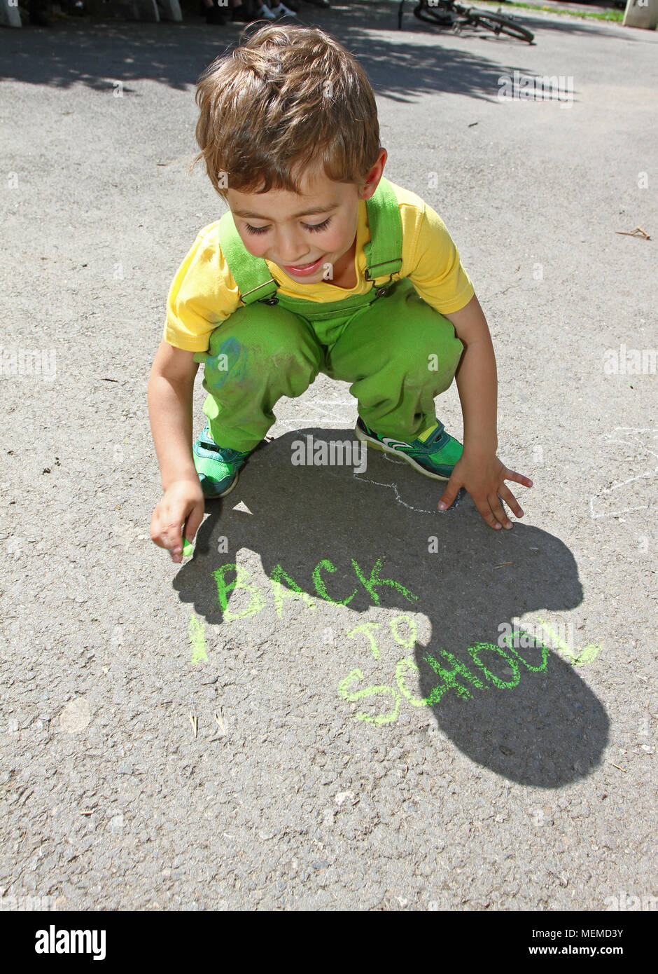 Ragazzo carino scrivere con gessi colorati su un parco giochi per bambini. Capretto piccolo disegna con gessi. Concetto di vacanza. Il concetto di istruzione. Scuola e tempo di divertimento. Giocare Foto Stock