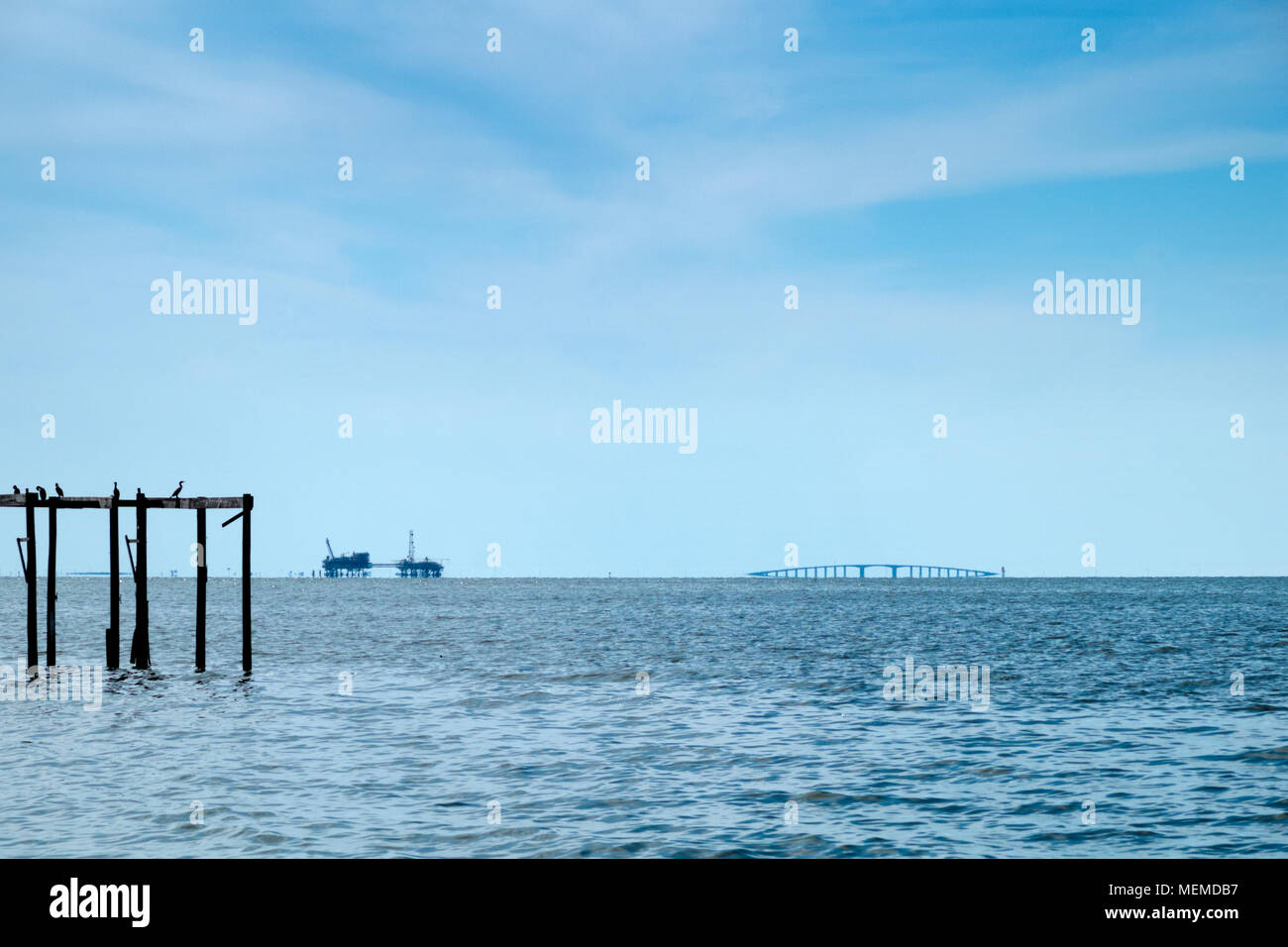 Nel tardo pomeriggio sulla Baia di Mobile, Alabama. Il gas naturale trivelle e Le Dauphin Island bridge sedersi all'orizzonte al di sotto di un azzurro intenso del cielo. Cormorani appollaiarsi su Foto Stock