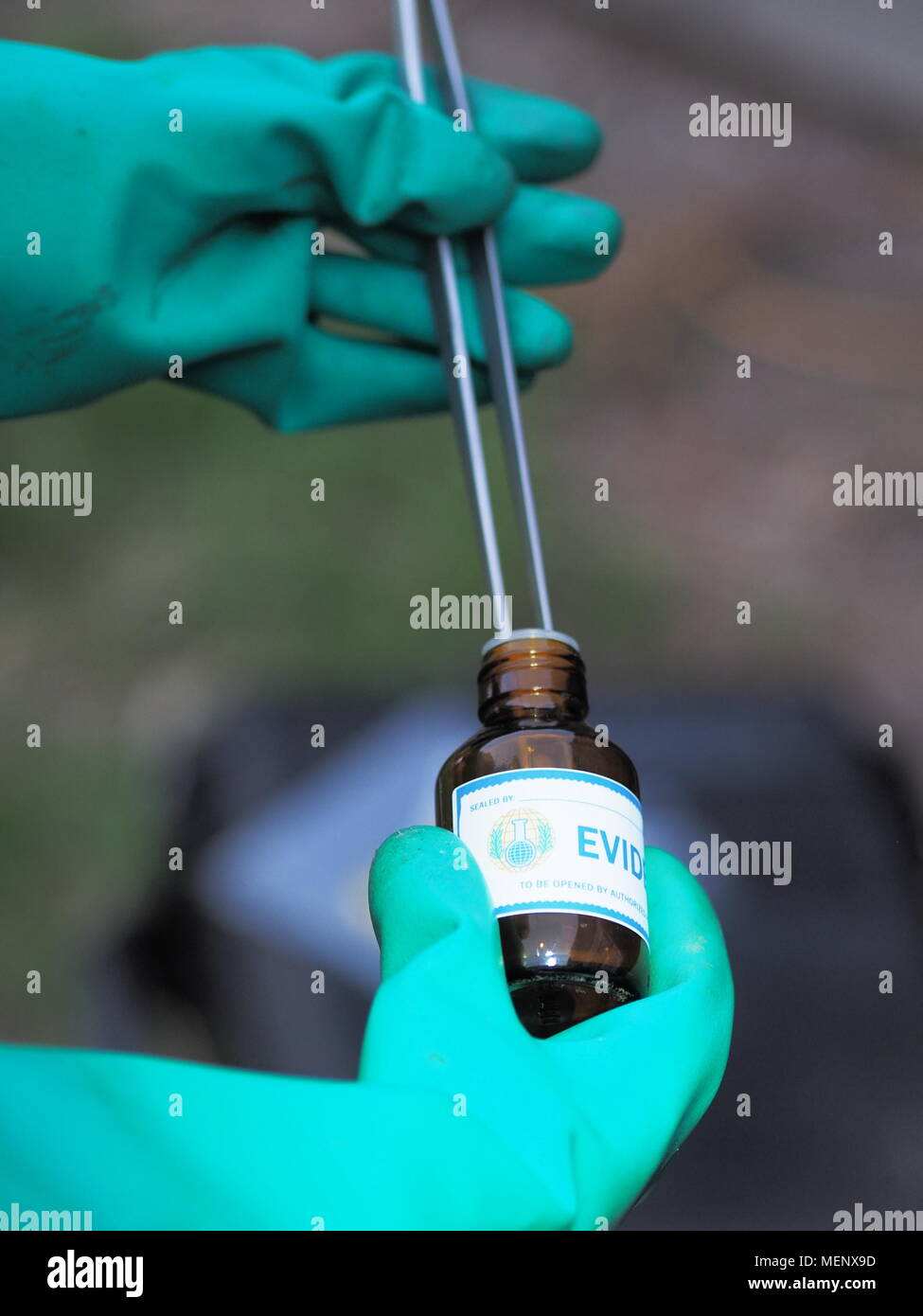 In mano i guanti di protezione inserti campione con lunghe pinze in evidenza un contenitore di stoccaggio. Foto Stock