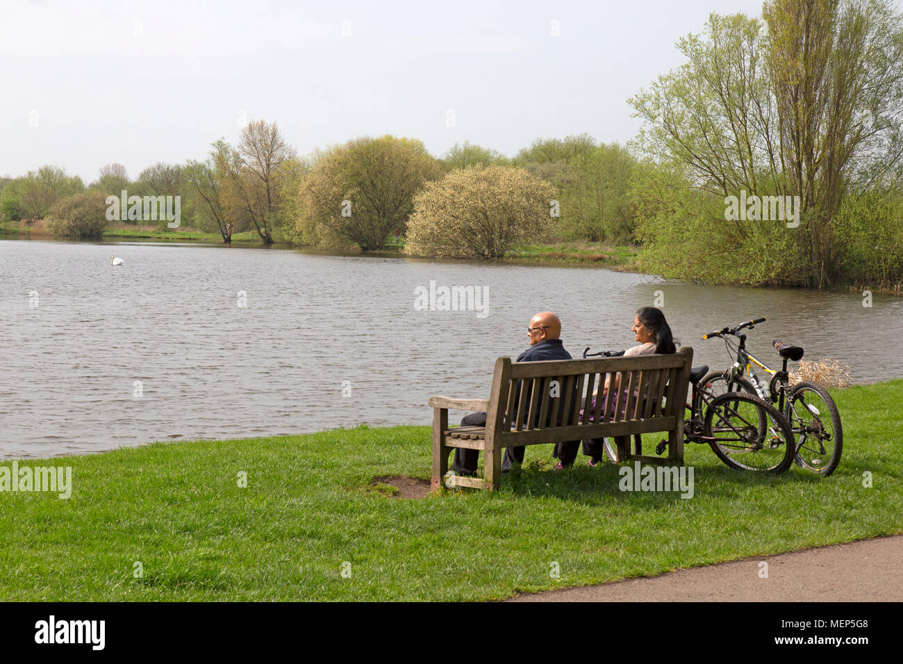 Watermead Country Park nel Leicestershire, in Inghilterra. Una coppia di mezza età su un banco di lavoro, prendendo una pausa dalle escursioni in bicicletta intorno ai laghi nel parco Foto Stock