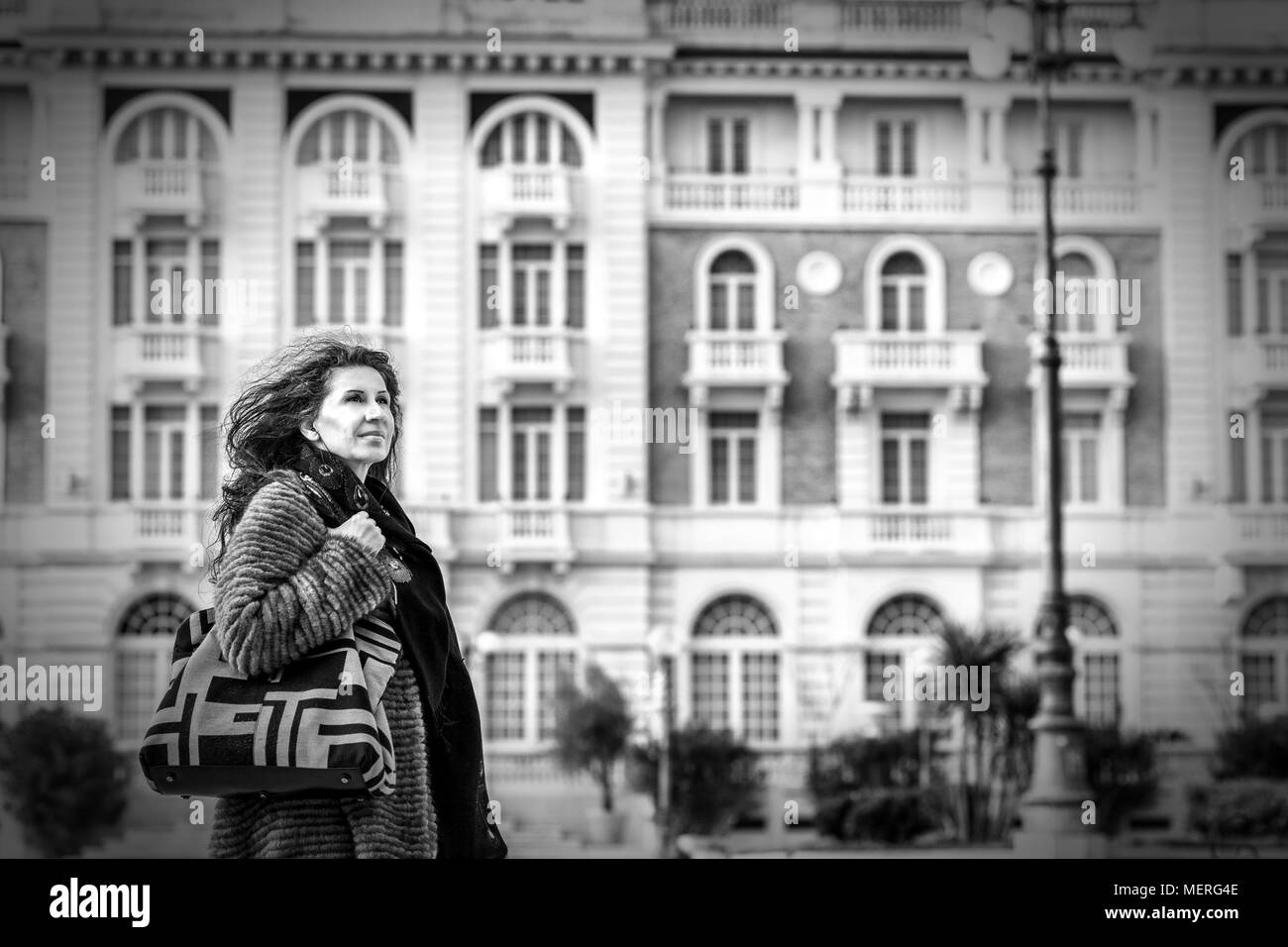 Donna matura a piedi con il vento nei capelli vicino antico edificio in background in Italia Foto Stock