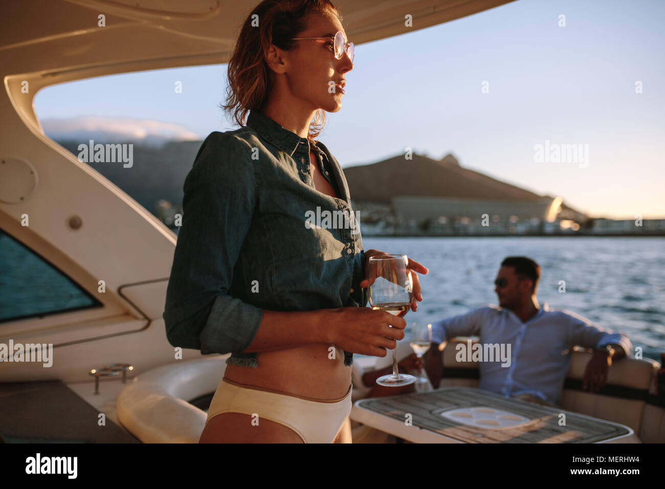 Donna attraente con un bicchiere di vino su yacht con gli amici seduti sul retro. Femmina su barca privata con amici in background. Foto Stock