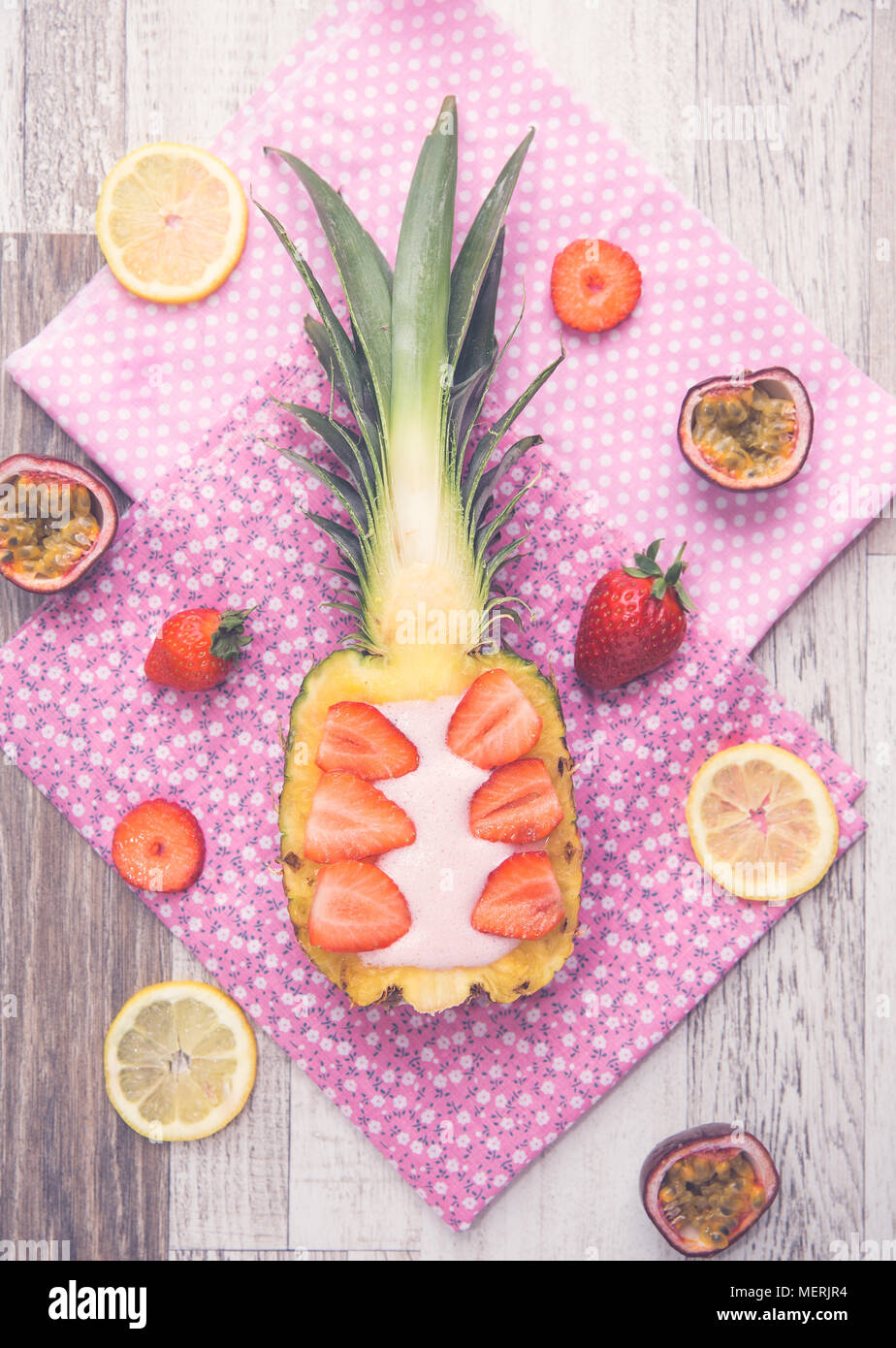 Guardando verso il basso a partire da sopra su un ananas e fragola smoothie che è stata servita all'interno di una metà di ananas e circondato dai suoi ingredienti. Foto Stock