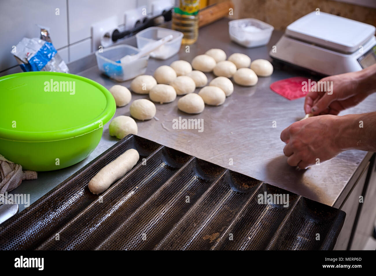 Un close-up di una femmina di bakerpulls l'impasto per la cottura di focacce di hotdog su un metallo becary tabella con un mattarello Foto Stock