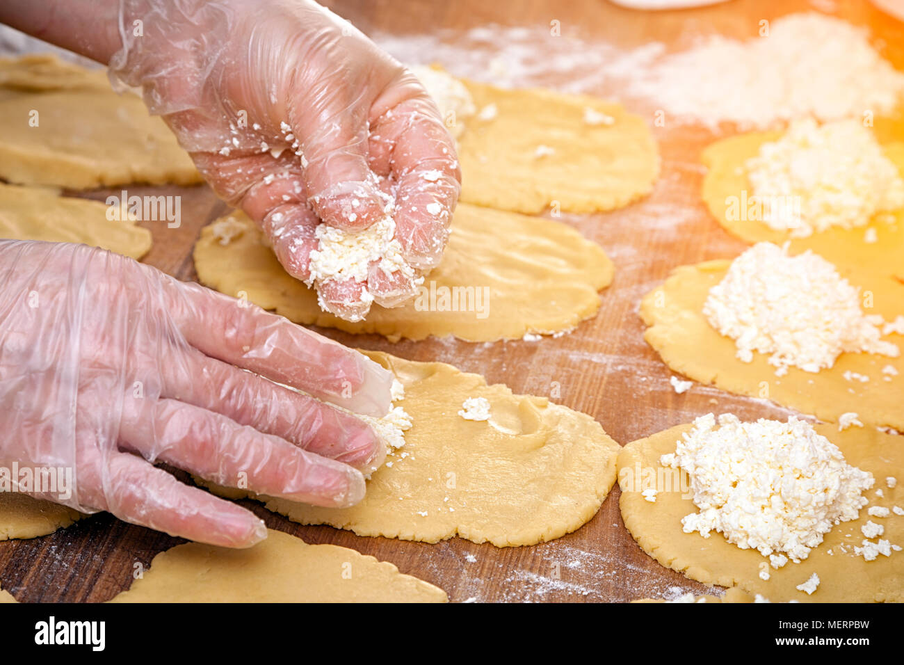 Un close-up di una femmina di baker in guanti protettivi tira fuori l'impasto per la cottura di focacce wiith formaggio su una tabella annodato con un mattarello Foto Stock