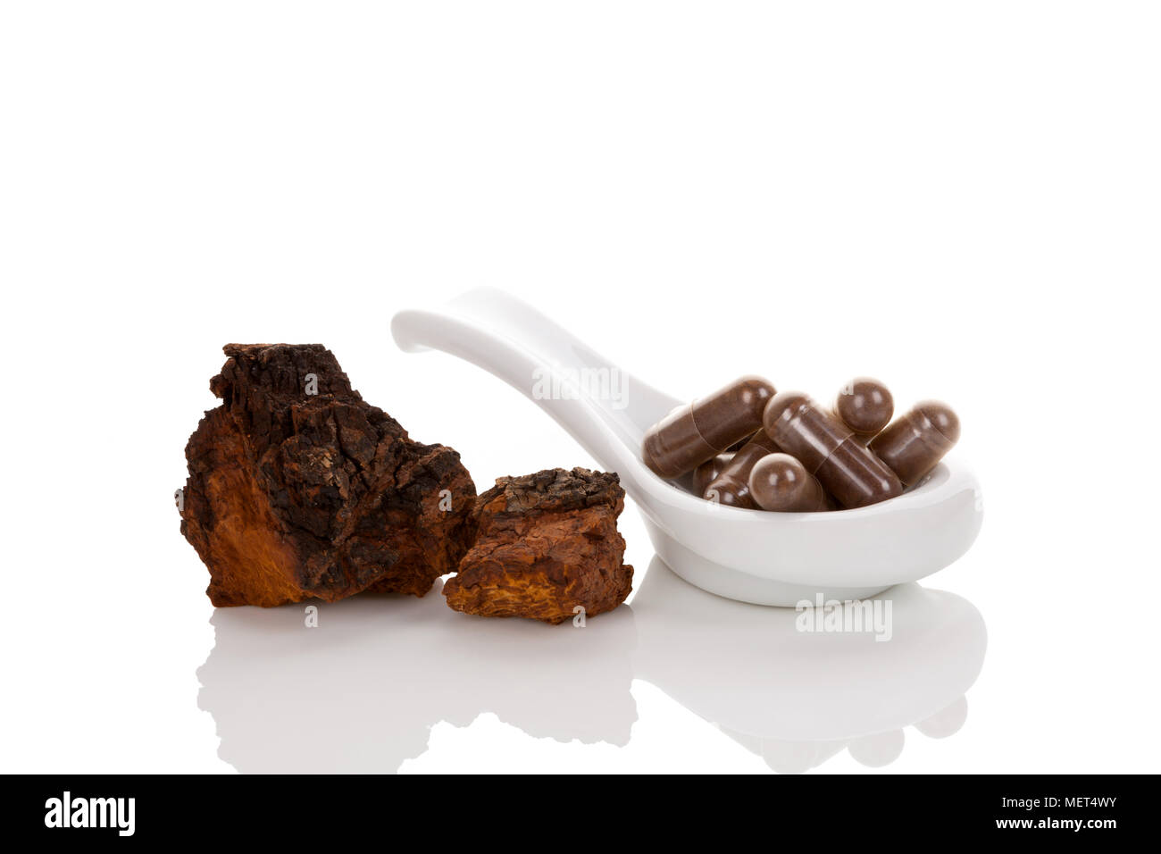 Inonotus obliquus, chaga pezzi e capsule di gel sul cucchiaio isolati su sfondo bianco. Fungo medicinale. Foto Stock