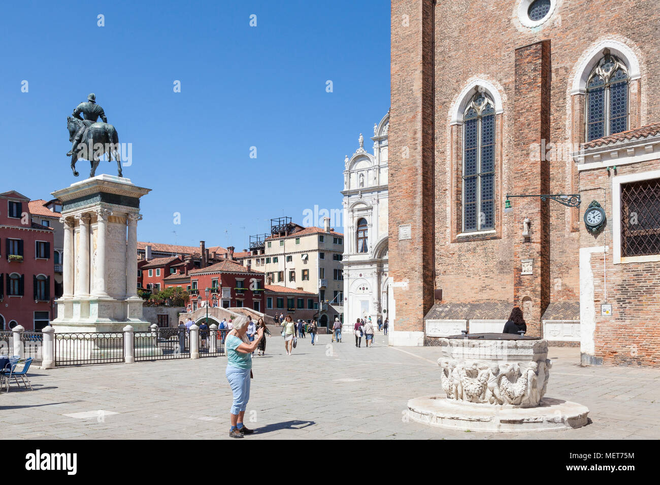 Donna anziana turista fotografando un pozzo medievale o testa pozzo, Campo Santi Giovanni e Paolo, Castello, Venezia, Veneto, Italia. Statua di Bartolomeo Foto Stock