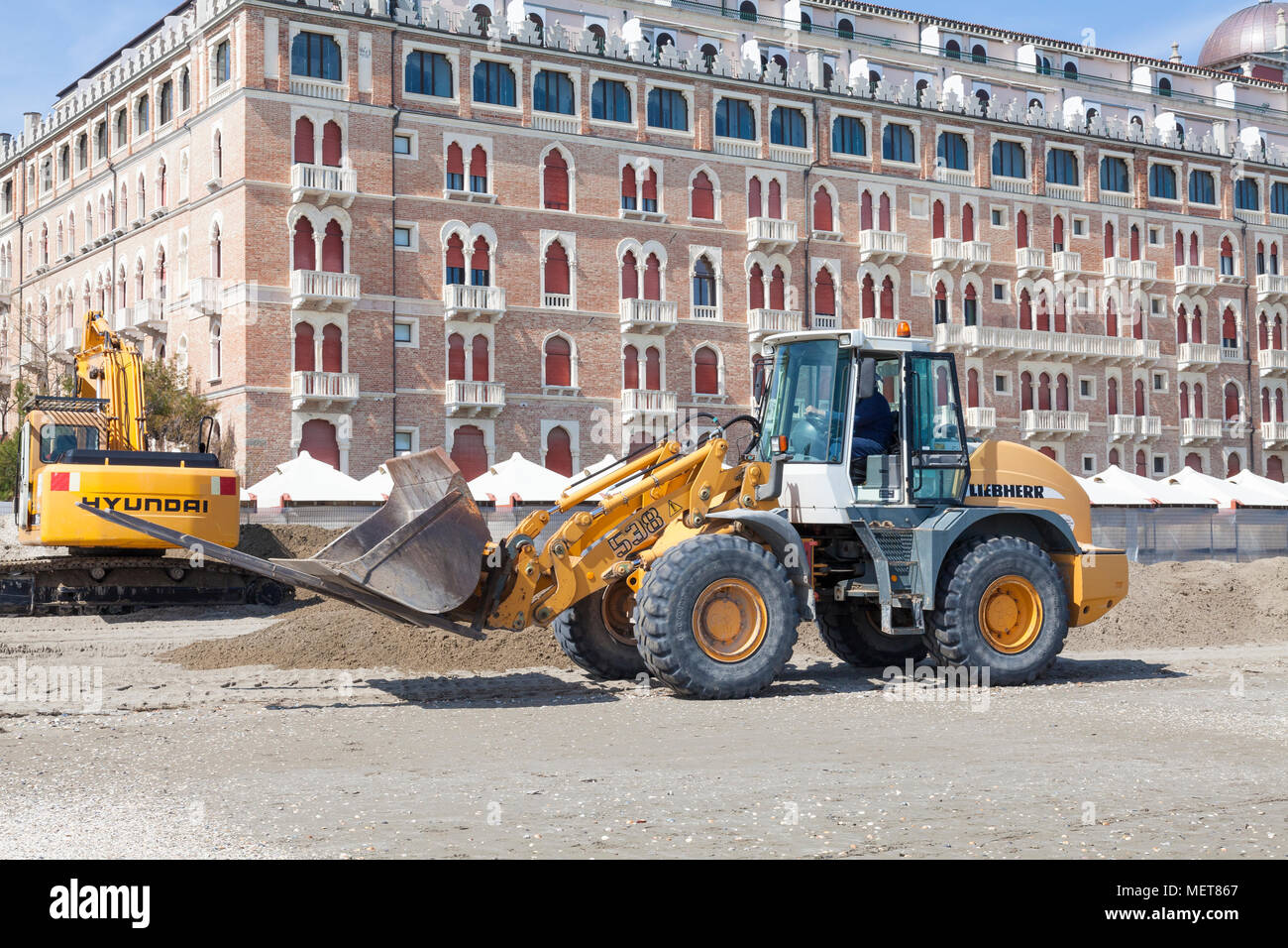 Operai preparando la spiaggia per la stagione estiva, Lido di Venezia, Venezia, Veneto, Italia usando un escavatore (Escavatore) e caricatore a estremità anteriore nella parte anteriore del Excel Foto Stock