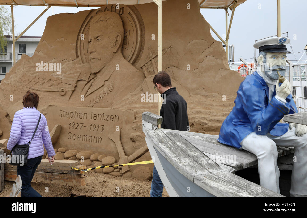 23 aprile 2018, Germania, Warnemuende: i visitatori dai un occhiata alla scultura di Andrey Molokov dalla Repubblica di Chuvash sul tema del mare dei soccorritori alla nona Warnemuende mondo di sabbia. Sei artisti provenienti da cinque paesi ha creato sculture fuori di circa 300 tonnellate di sabbia sul tema della 'Die geheimnisvolle Stadt - 800 Jahre Rostock' (lit. La città misteriosa - 800 anni di Rostock). Foto: Bernd Wüstneck/dpa Foto Stock