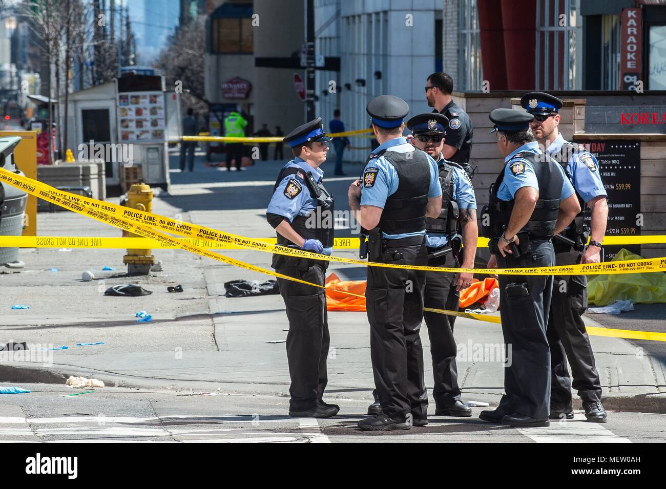 Toronto, Ontario, Canada. 23 apr, 2018. Gli ufficiali di polizia a stare di fronte ad un corpo coperto di Toronto dopo un van montato un marciapiede di schiantarsi in un certo numero di pedoni il lunedì. Nove persone sono state uccise e almeno 16 altri feriti dopo un camioncino bianco entra in collisione con i pedoni a Yonge e Finch a nord del centro cittadino. Hanno detto le autorità il van è stata trovata e il conducente era in stato di custodia cautelare. Credito: Victor Biro/ZUMA filo/Alamy Live News Foto Stock
