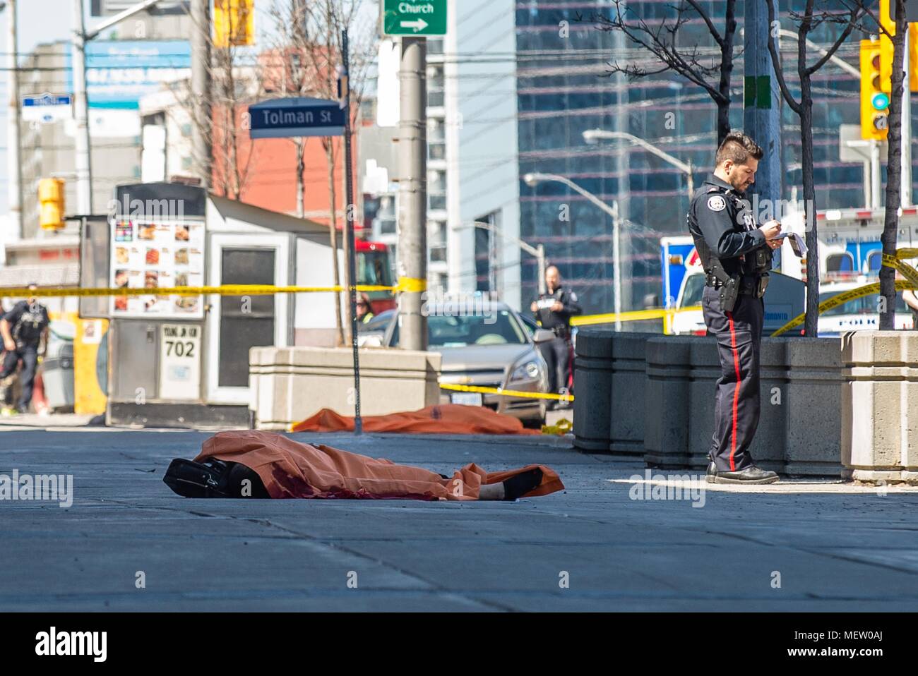 Toronto, Ontario, Canada. 23 apr, 2018. Un funzionario di polizia si erge nei pressi di un corpo coperto di Toronto dopo un van montato un marciapiede di schiantarsi in un certo numero di pedoni il lunedì. Nove persone sono state uccise e almeno 16 altri feriti dopo un camioncino bianco entra in collisione con i pedoni a Yonge e Finch a nord del centro cittadino. Hanno detto le autorità il van è stata trovata e il conducente era in stato di custodia cautelare. Credito: Victor Biro/ZUMA filo/Alamy Live News Foto Stock
