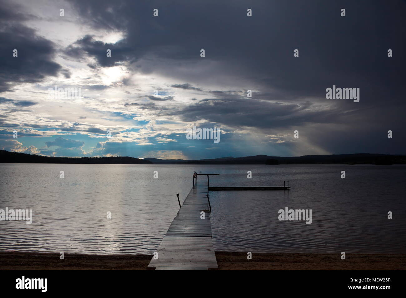 Un asse di legno conduce a ponte su un lago su una soleggiata giornata estiva con imponenti e nuvole drammatico Foto Stock