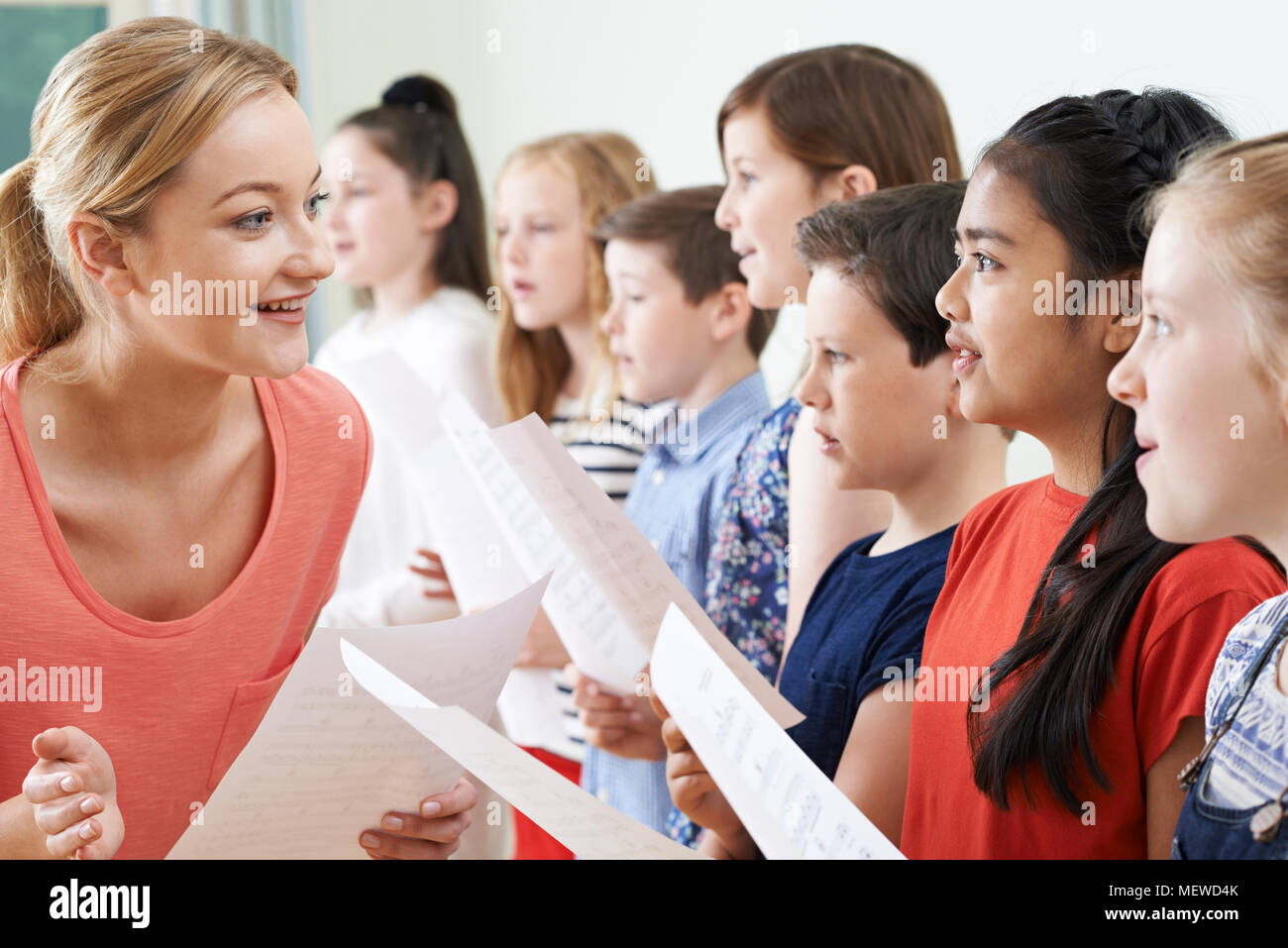 I bambini in coro scolastico essendo incoraggiati dall'insegnante Foto Stock