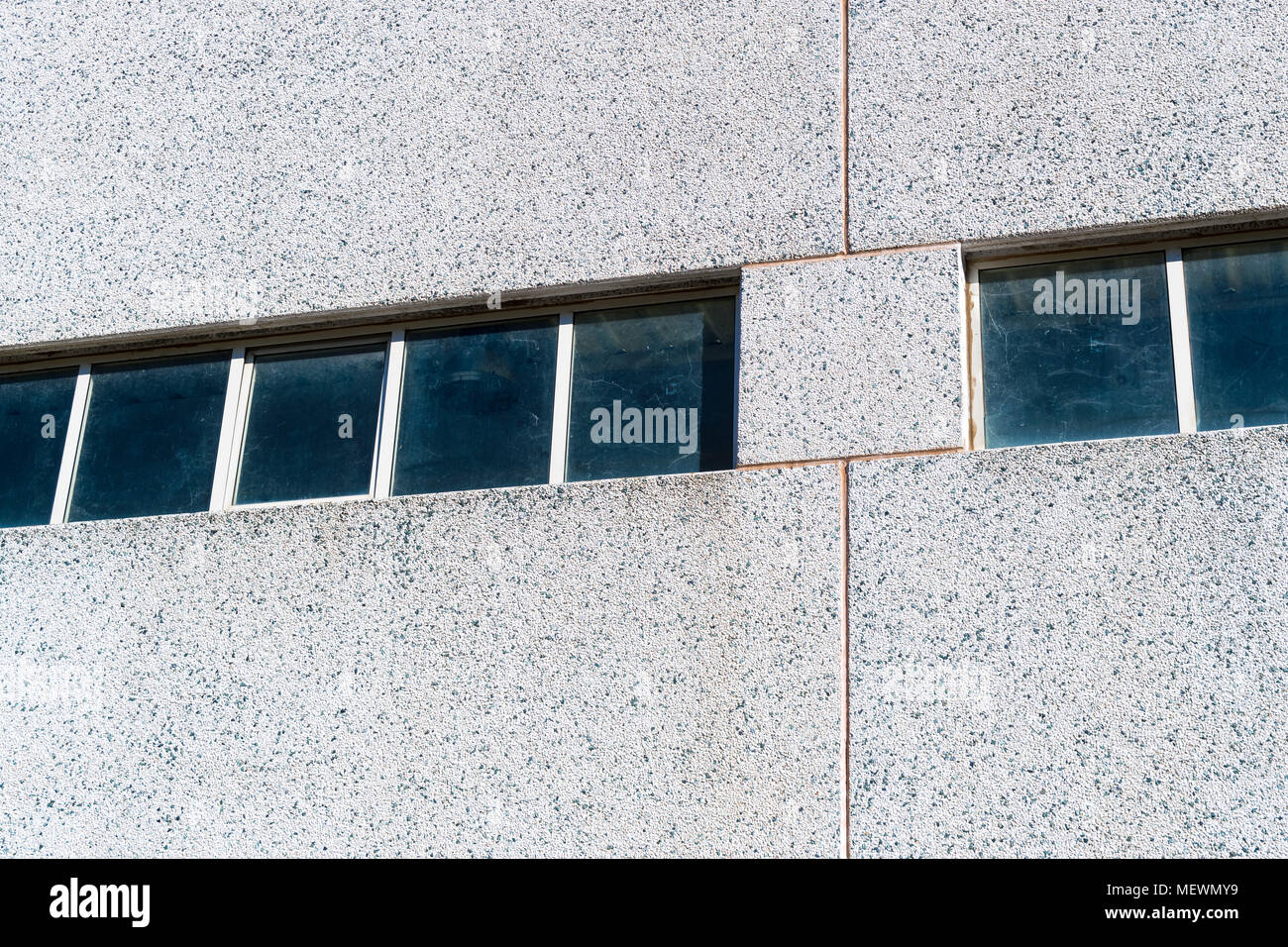 Una fila di finestre sul muro grigio di un capannone industriale Foto Stock