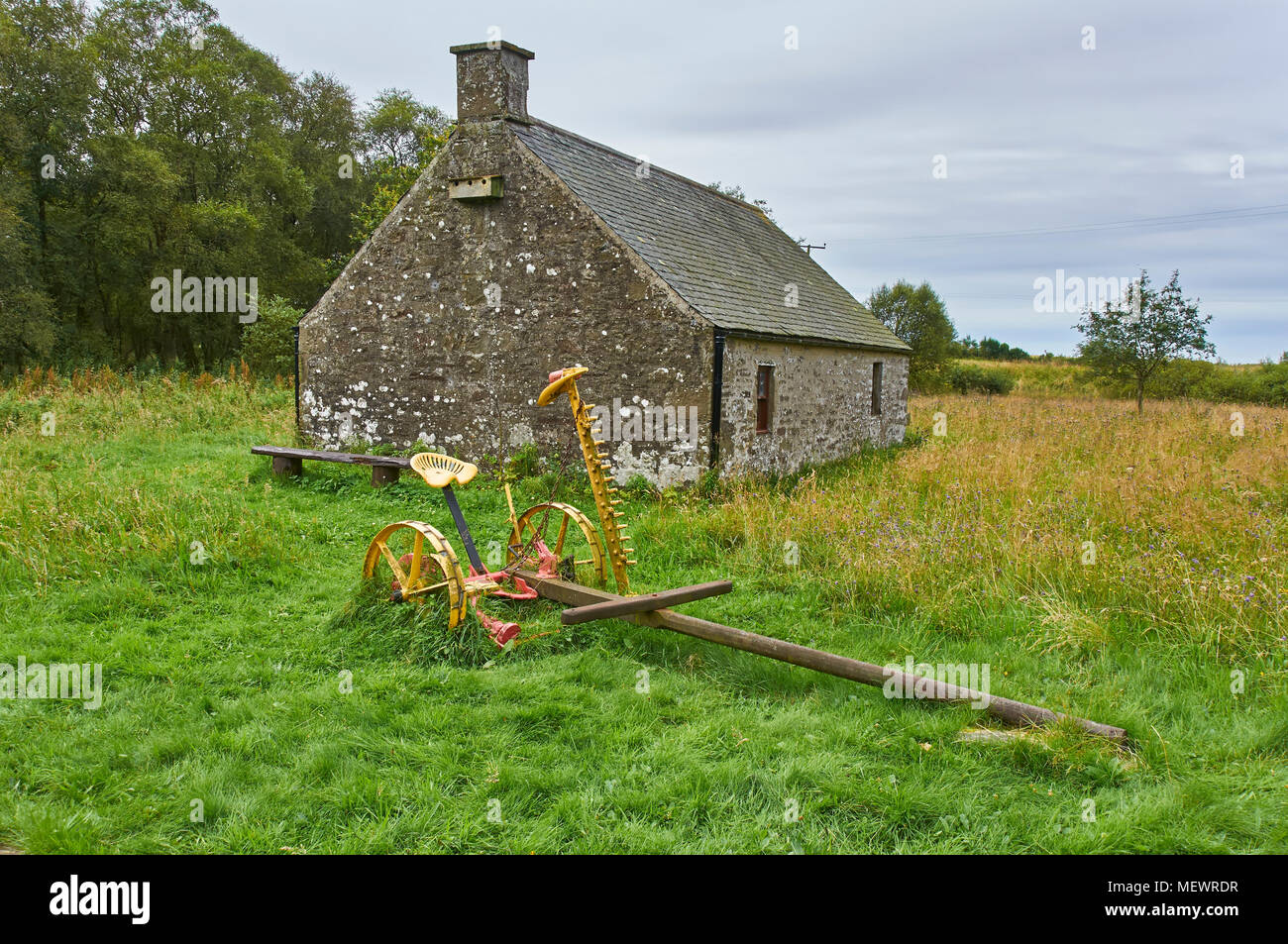 Un piccolo cottage con un antico Cavallo e fieno cutter parcheggiato al di fuori di essa, a Crombie parco vicino a Dundee in Angus, Scozia. Foto Stock