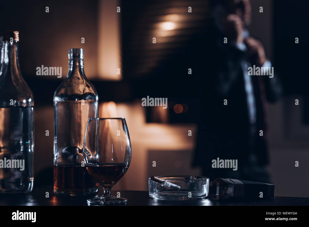Bottiglia di vetro con alcool e sigarette con un imprenditore in background Foto Stock