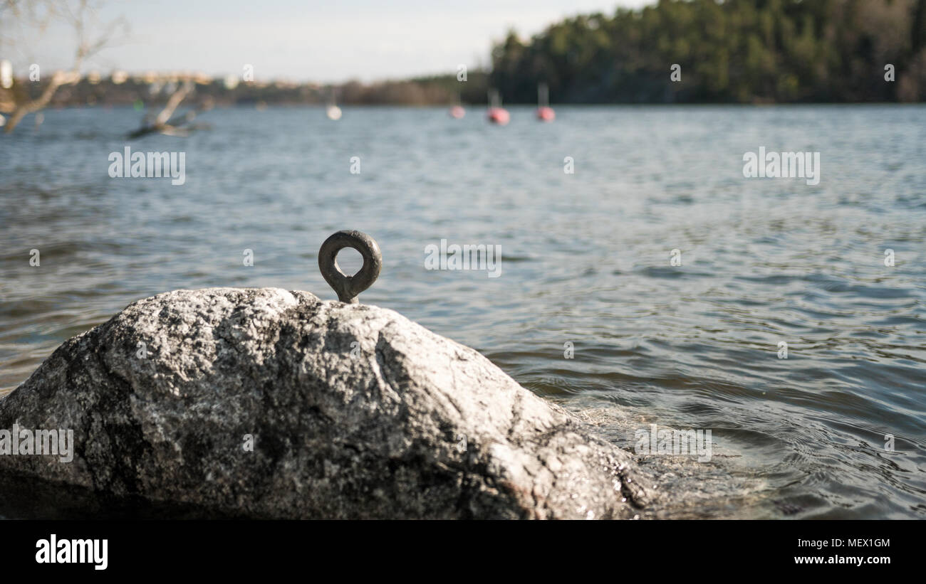 Anello metallico per barca fune fissare all'interno di una roccia dalle sponde del lago. Foto Stock