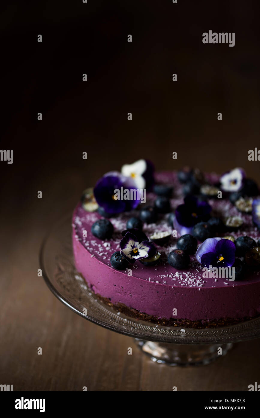 Materie mirtillo torta sul supporto decorato con mirtilli e fiori commestibili. Moody illuminazione. Spazio per la copia. Foto Stock