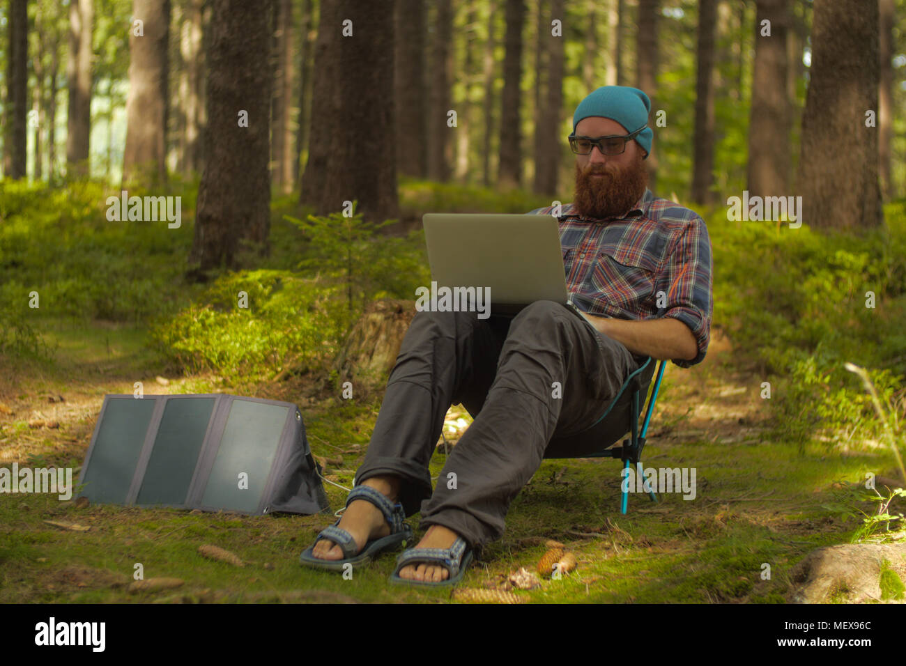 Il nomade digitale, giovane uomo caucasico lavorando sul suo laptop seduto su una sedia da campeggio nei boschi, backpacking, Foto Stock