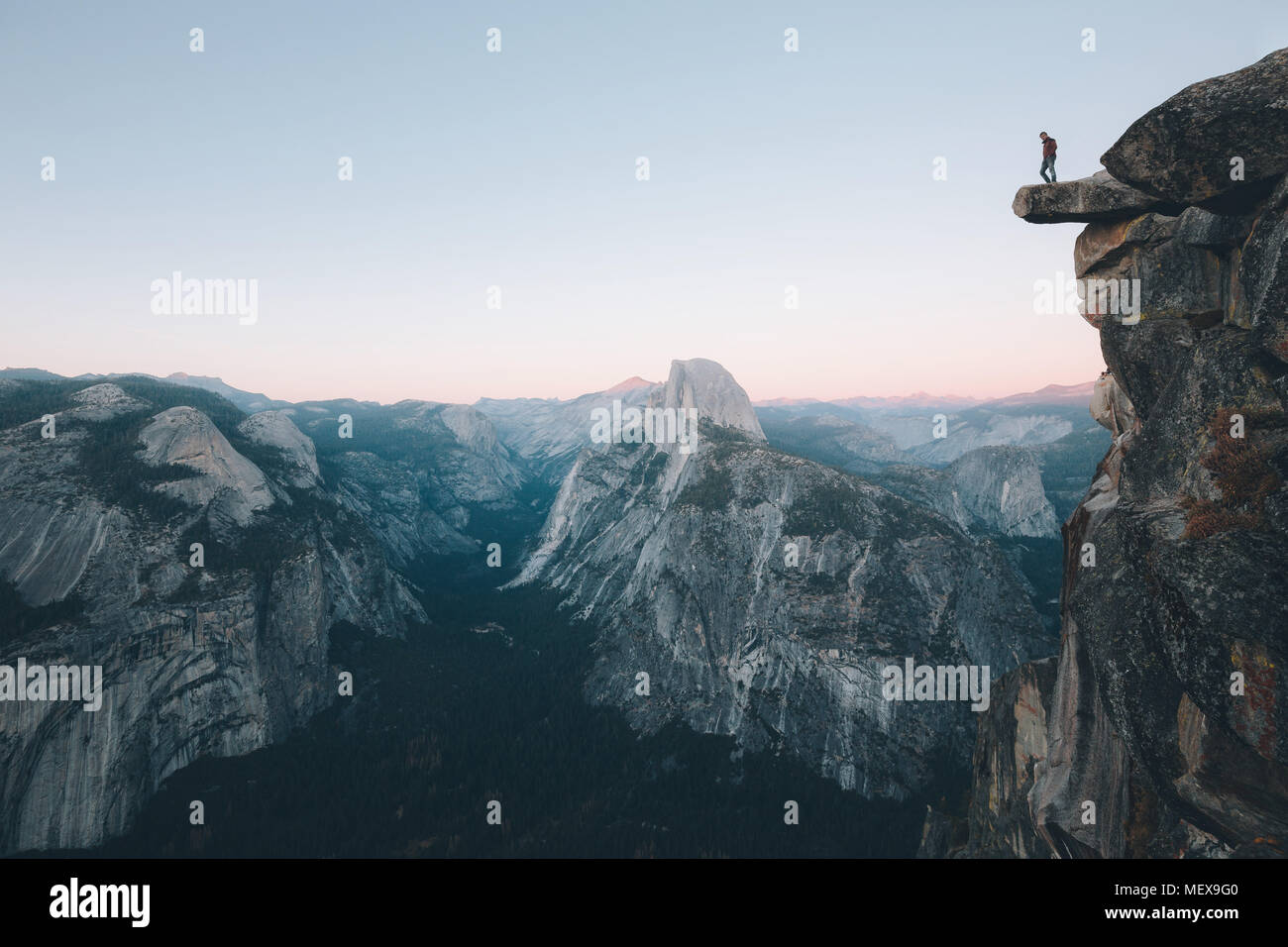 Un intrepido escursionista è in piedi su una roccia a strapiombo godendo della vista verso il famoso Half Dome presso il Glacier Point si affacciano, Yosemite National Park, STATI UNITI D'AMERICA Foto Stock