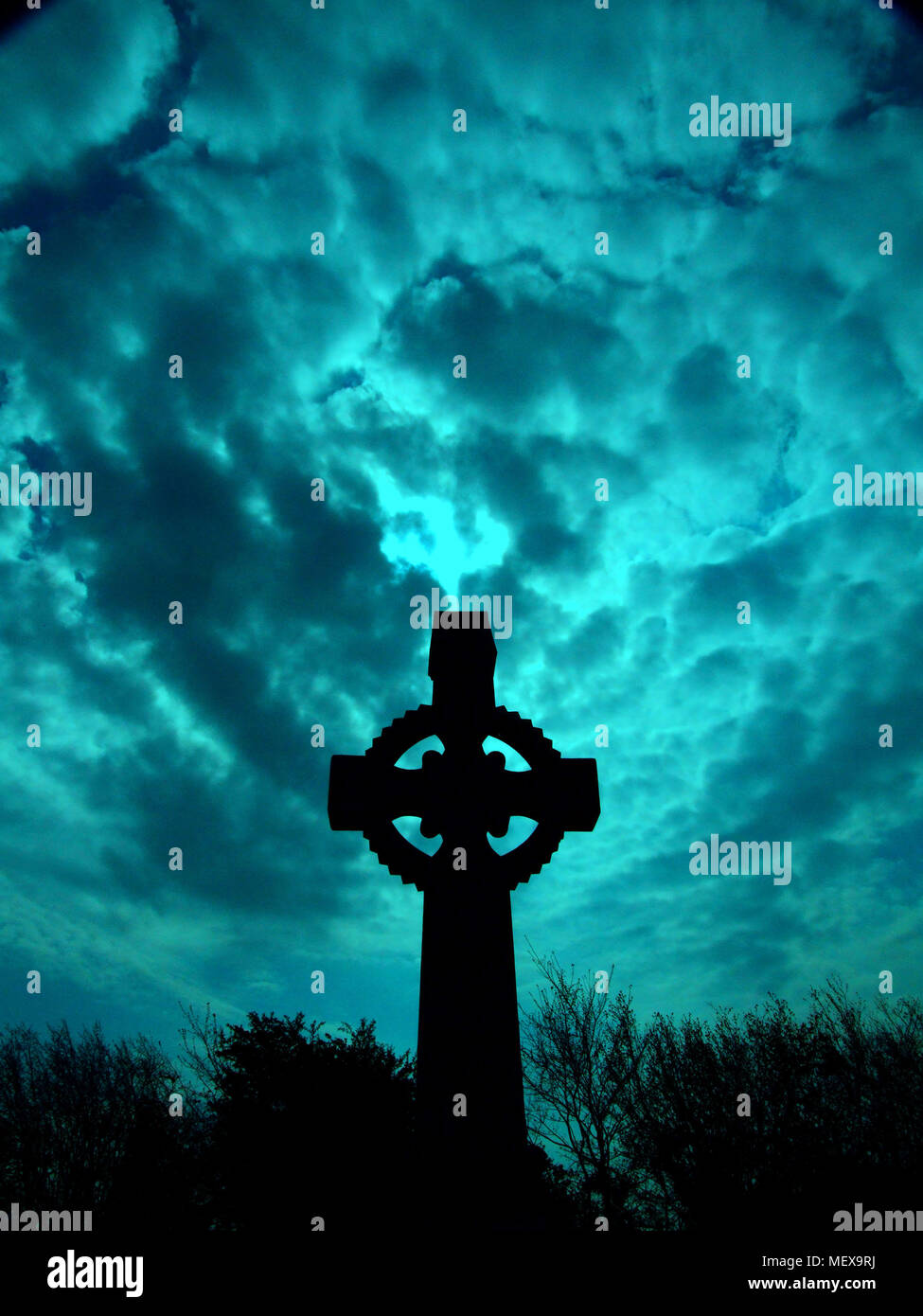 Croce celtica da un angolo basso con le nuvole di una tonalità di blu galleggiante sopra Foto Stock