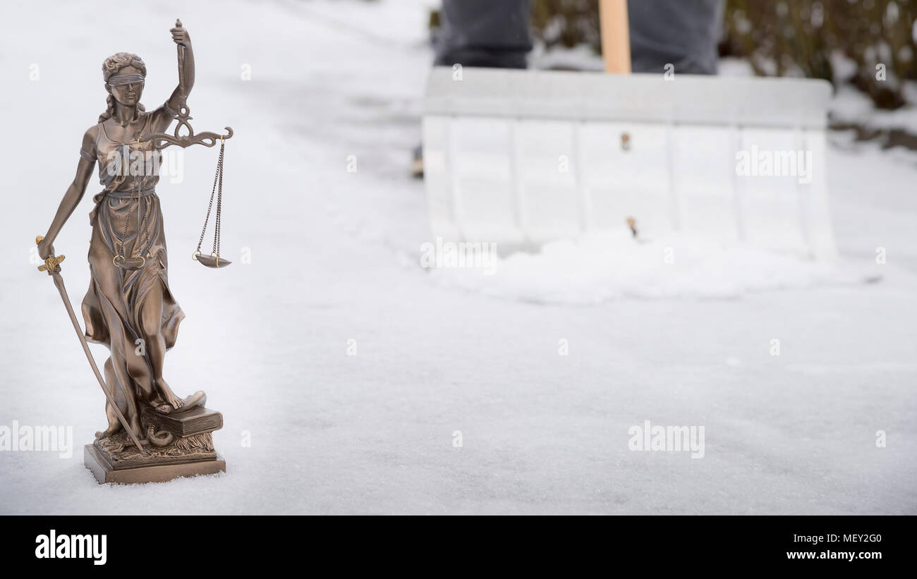 Quando dovete cancellare la neve? - Justitia statua in primo piano e sullo sfondo di un uomo è la rimozione di neve fuori sul marciapiede Foto Stock