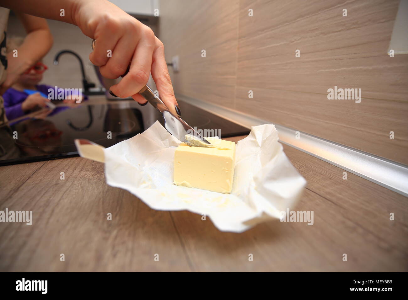 La cucina è casalinga sfondo. Close-up di donna di taglio mano burro fresco. Foto Stock