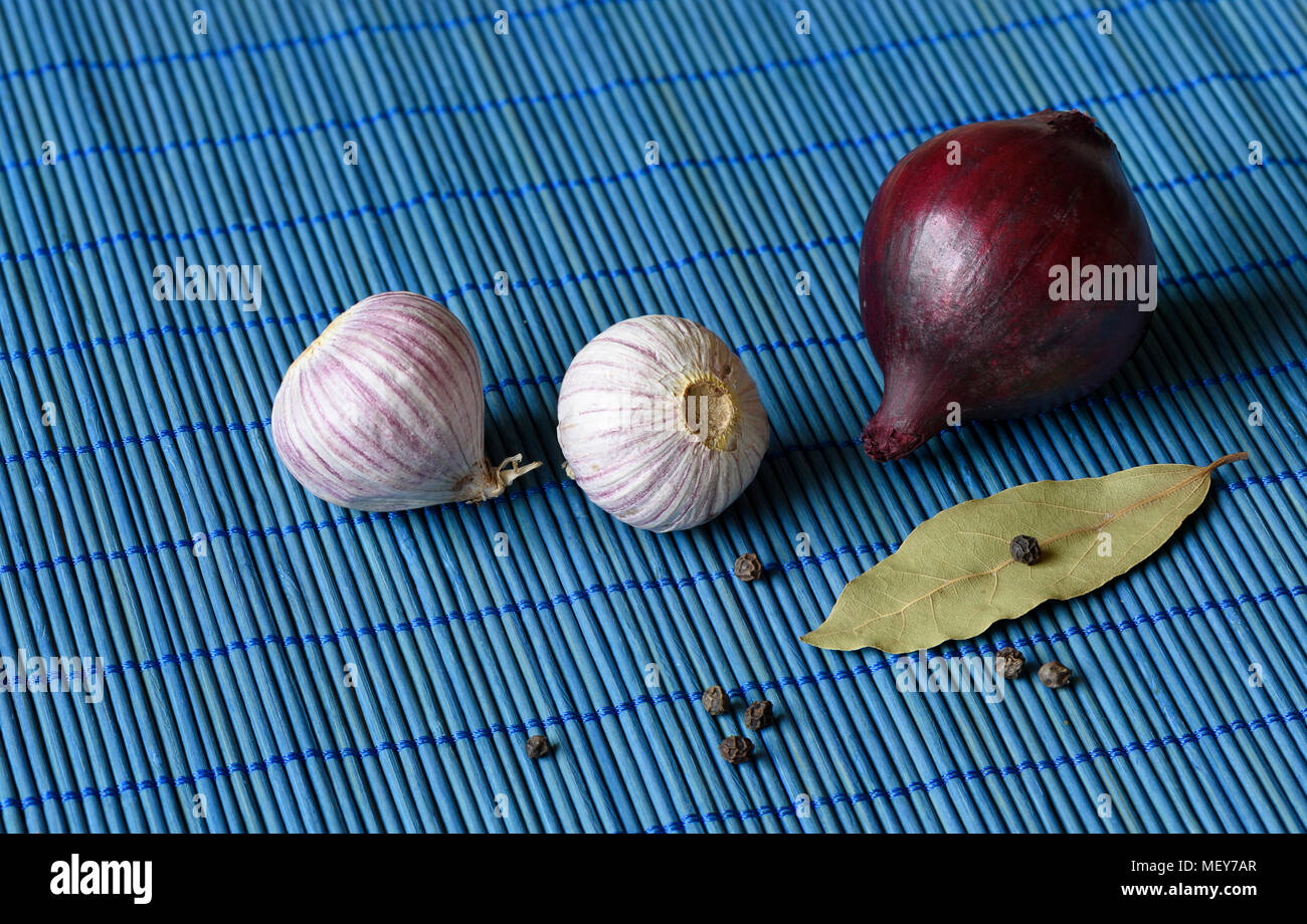 Aglio, cipolla rossa, la foglia di alloro con pepe su un tappetino sfondo Foto Stock