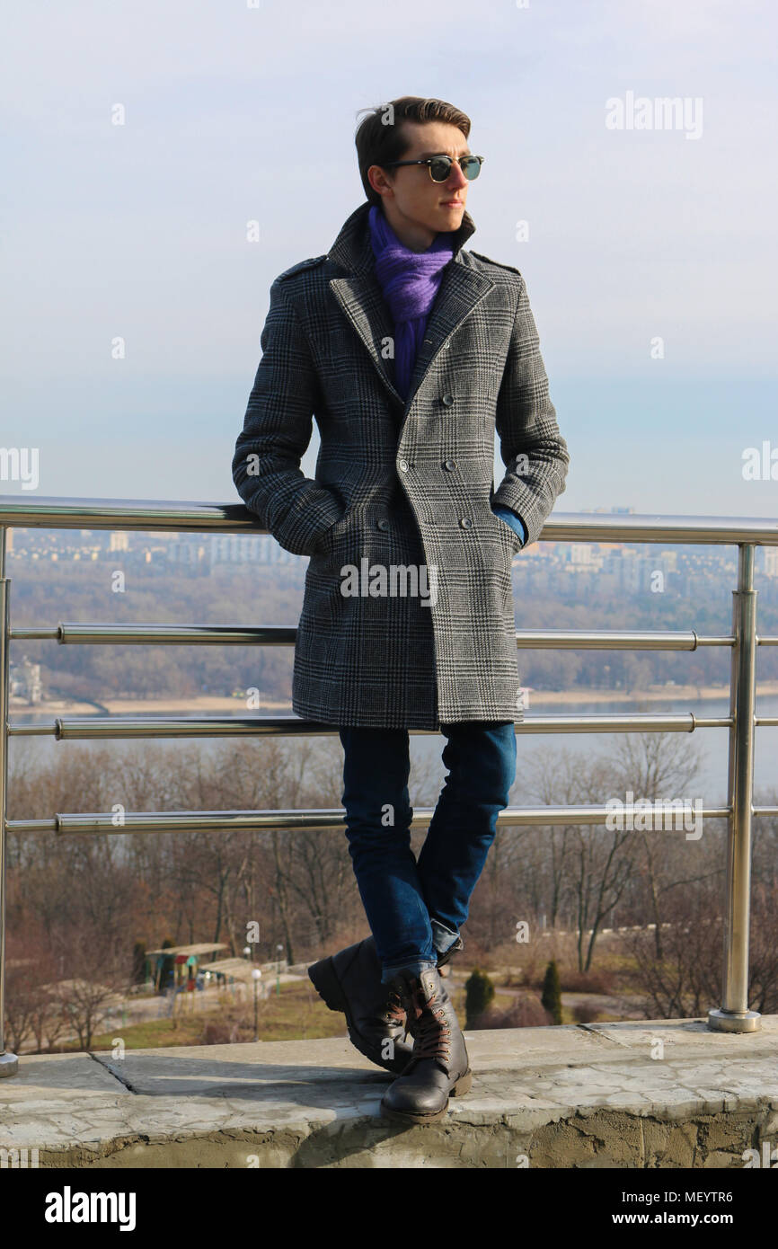 Il ritratto di un bel giovane hipster in occhiali neri, che sta guardando a sinistra un in piedi sul ponte in un parco. Tempo soleggiato. Foto Stock