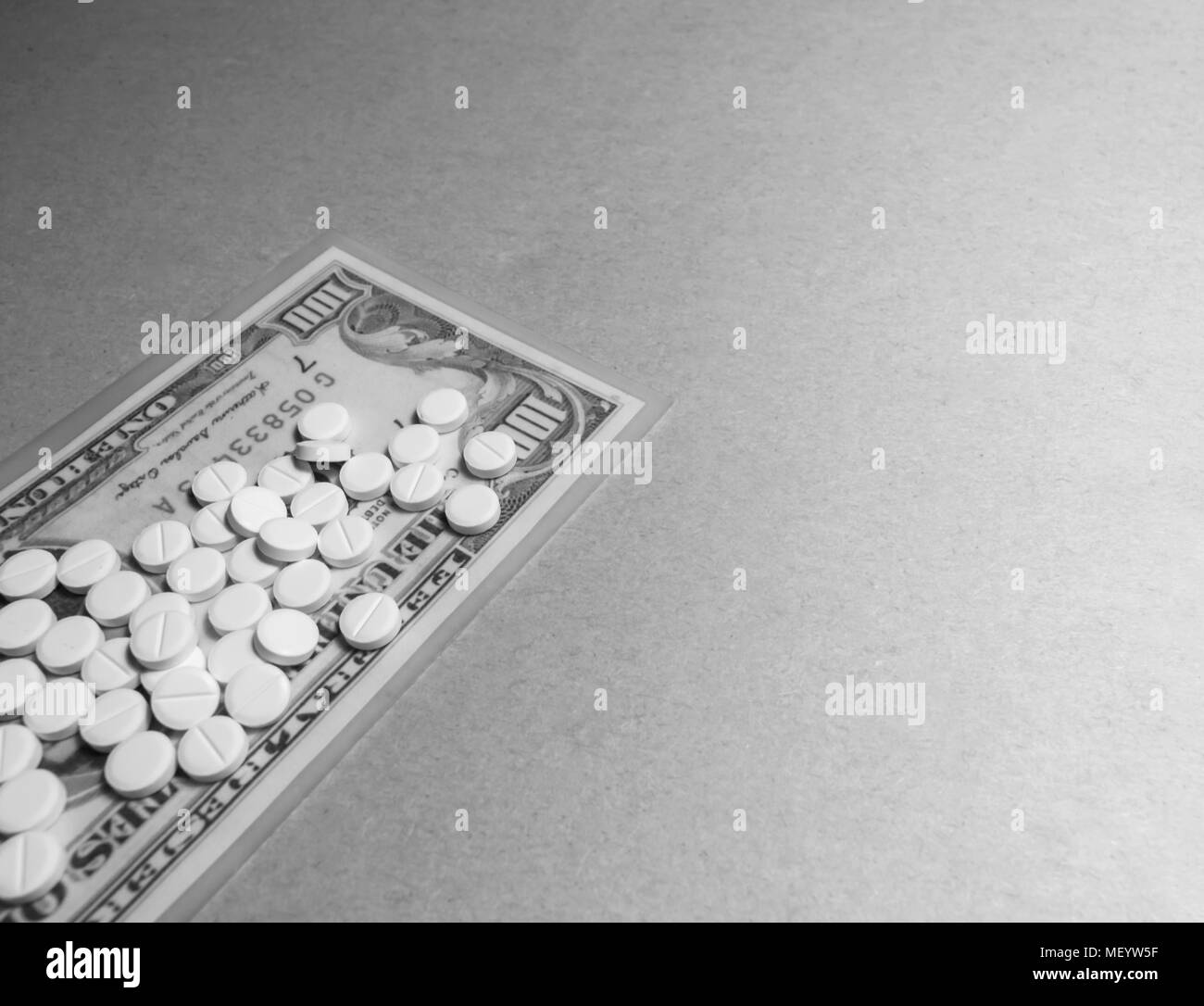 Una foto in bianco e nero di compresse su un centinaio di dollari su uno sfondo grigio con spazio di copia Foto Stock