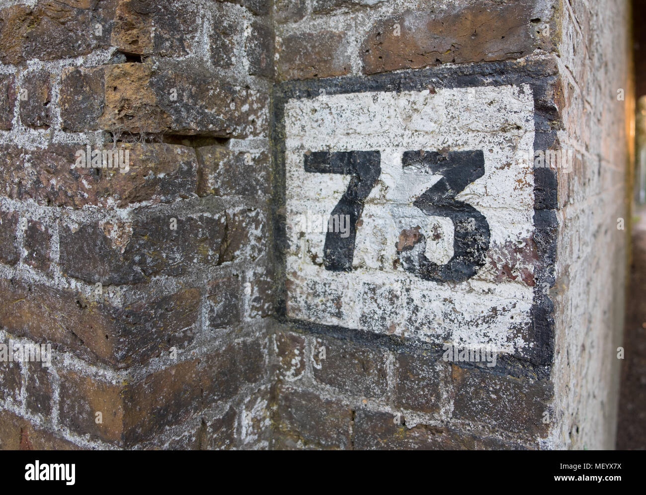 Dipinto il numero 73 sul vecchio muro in mattoni. Foto Stock