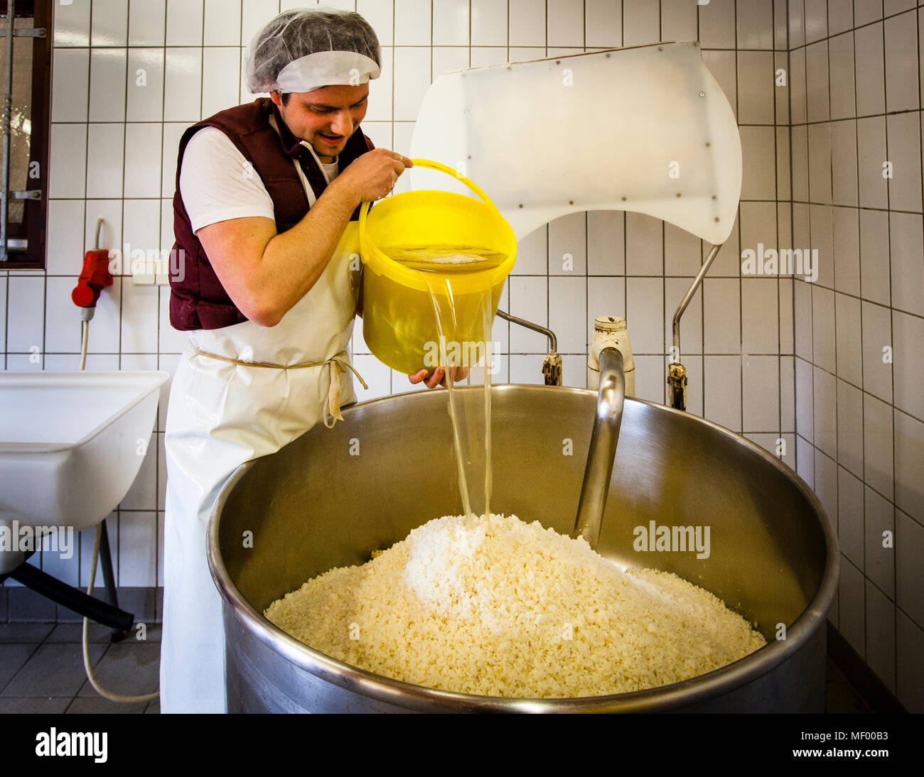Peter Koch versa acqua da un secchio giallo sui cereali macinati in un grande contenitore in acciaio inossidabile nel suo laboratorio di miso a Geisingen, Germania – il passo successivo prima di cuocere la massa. Foto Stock