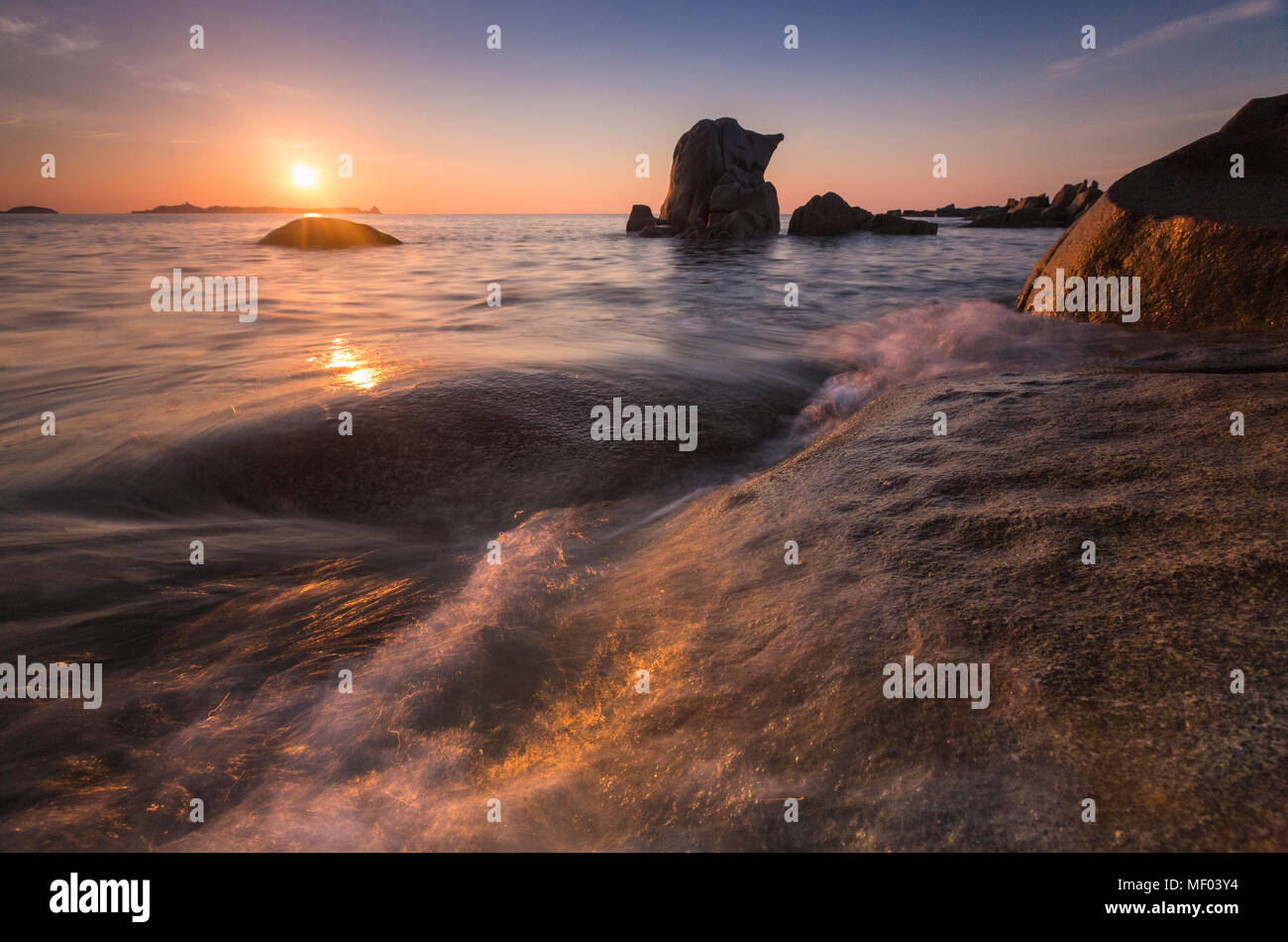 Le onde che si infrangono sulle rocce sotto il cielo fiery presso sunrise Punta Molentis Villasimius Cagliari Sardegna Italia Europa Foto Stock