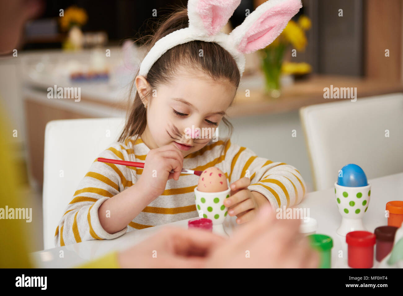 Ragazza con orecchie di coniglietto seduta a tavola di pittura delle uova di Pasqua Foto Stock