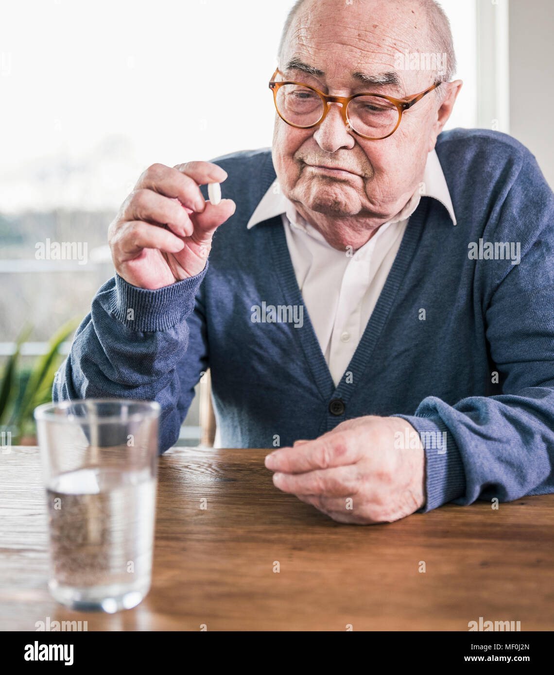 Ritratto di senior uomo seduto a tavola con la pillola e bicchiere di acqua Foto Stock