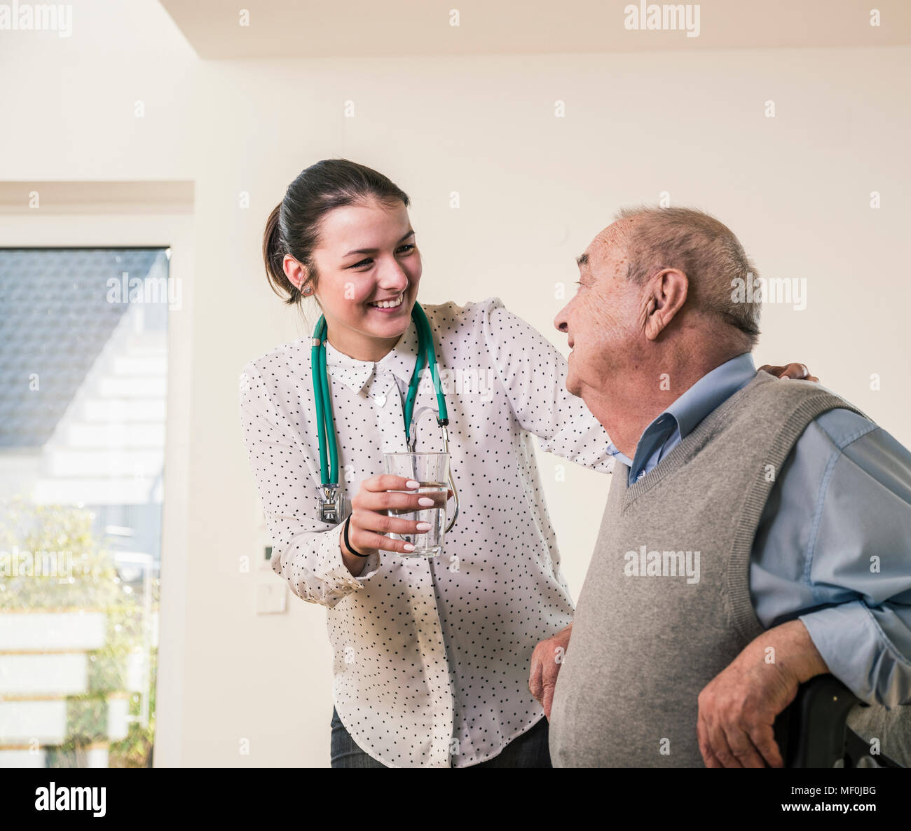Senior uomo sorridente a infermiere di vetro di contenimento di acqua a casa Foto Stock