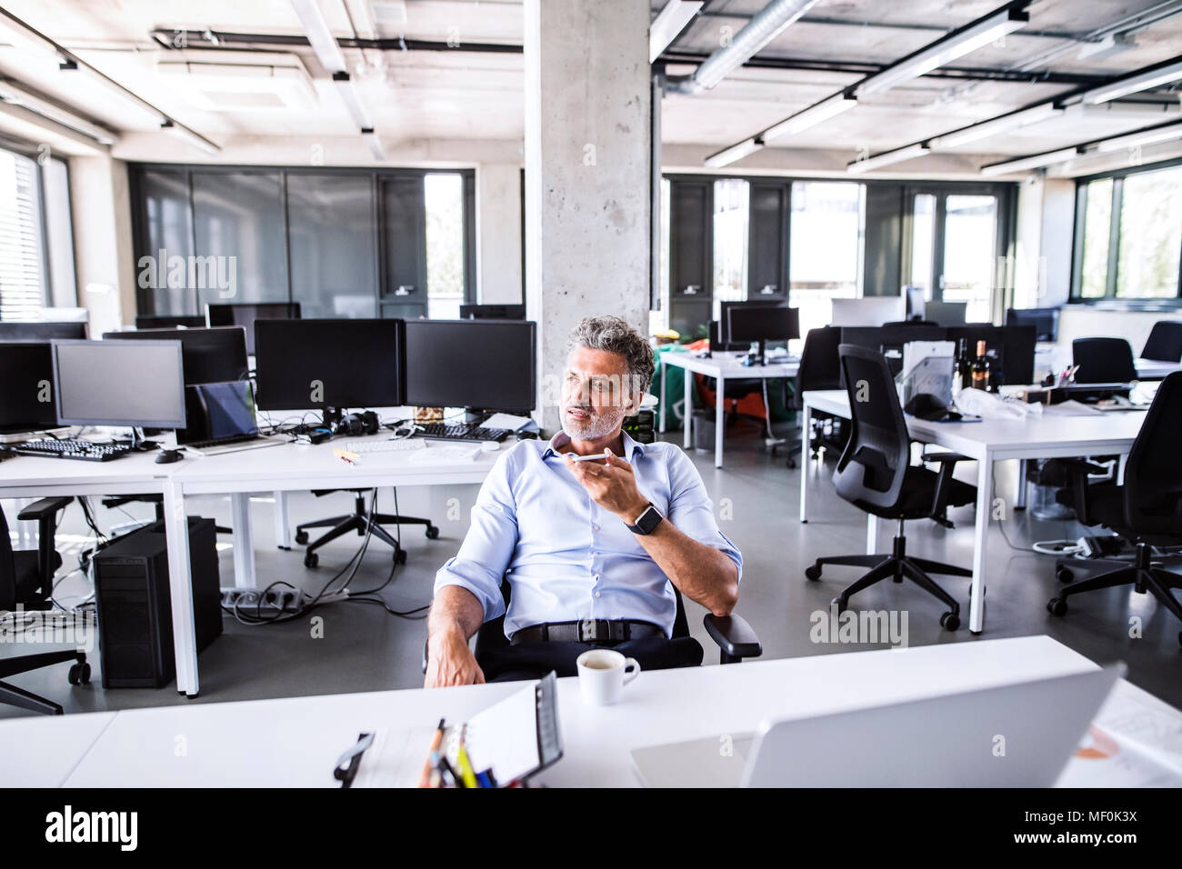 Imprenditore maturo seduto alla scrivania in ufficio utilizza lo smartphone Foto Stock