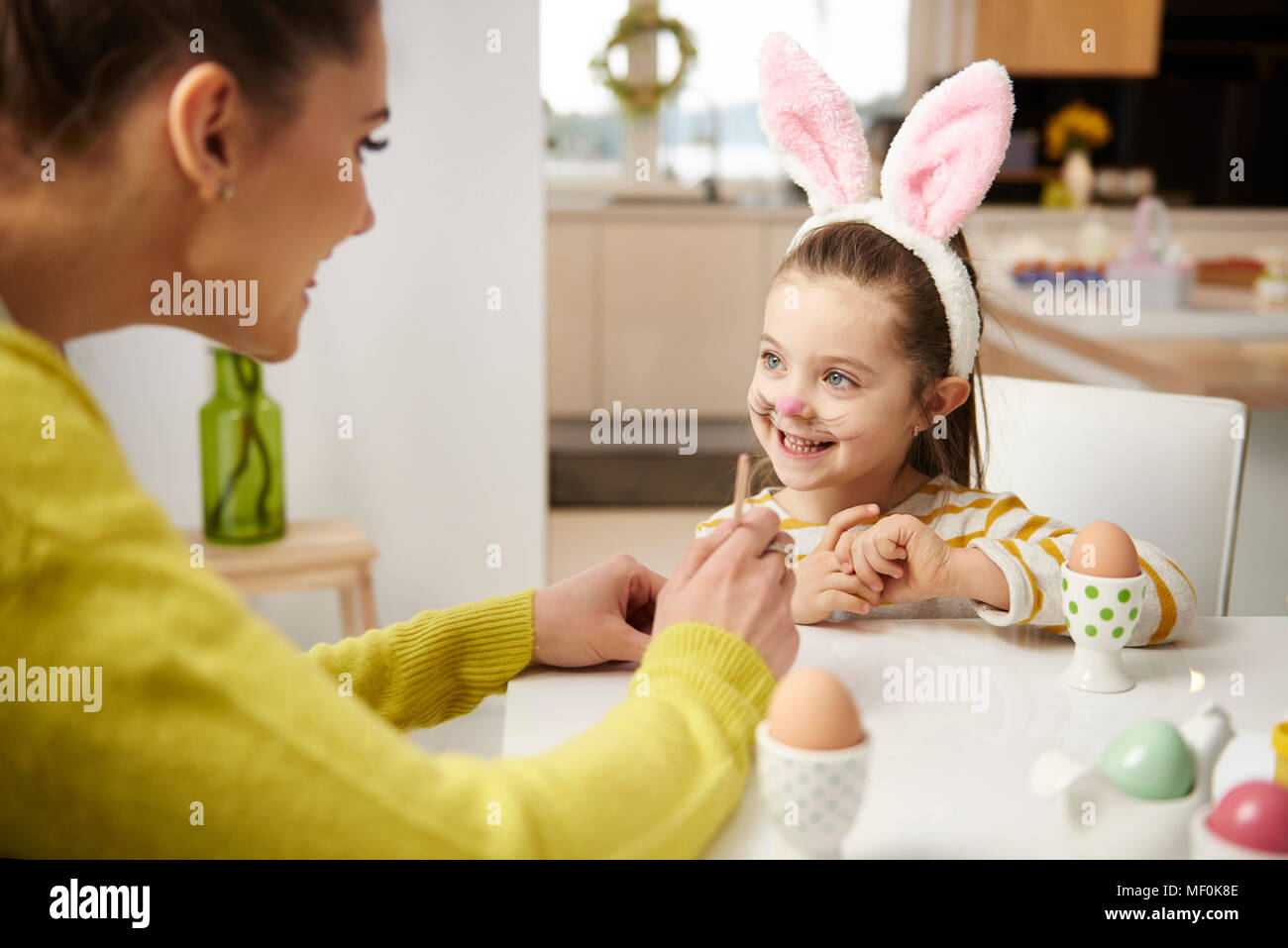 Ragazza con orecchie di coniglietto e madre seduta a tavola con le uova di Pasqua Foto Stock