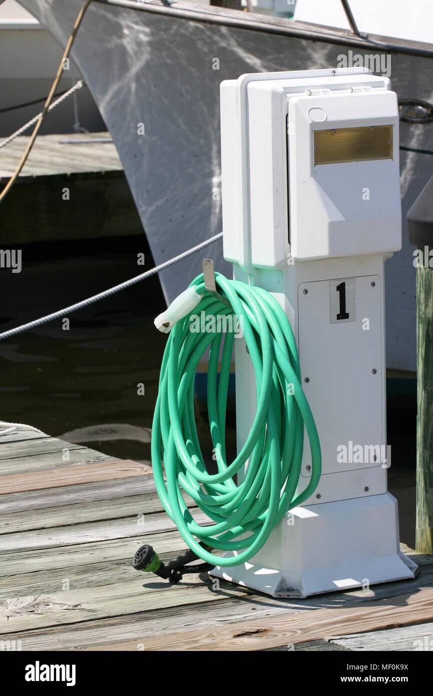 Un flessibile verde avvolto su un molo o pontile in attesa di lavare una barca Foto Stock