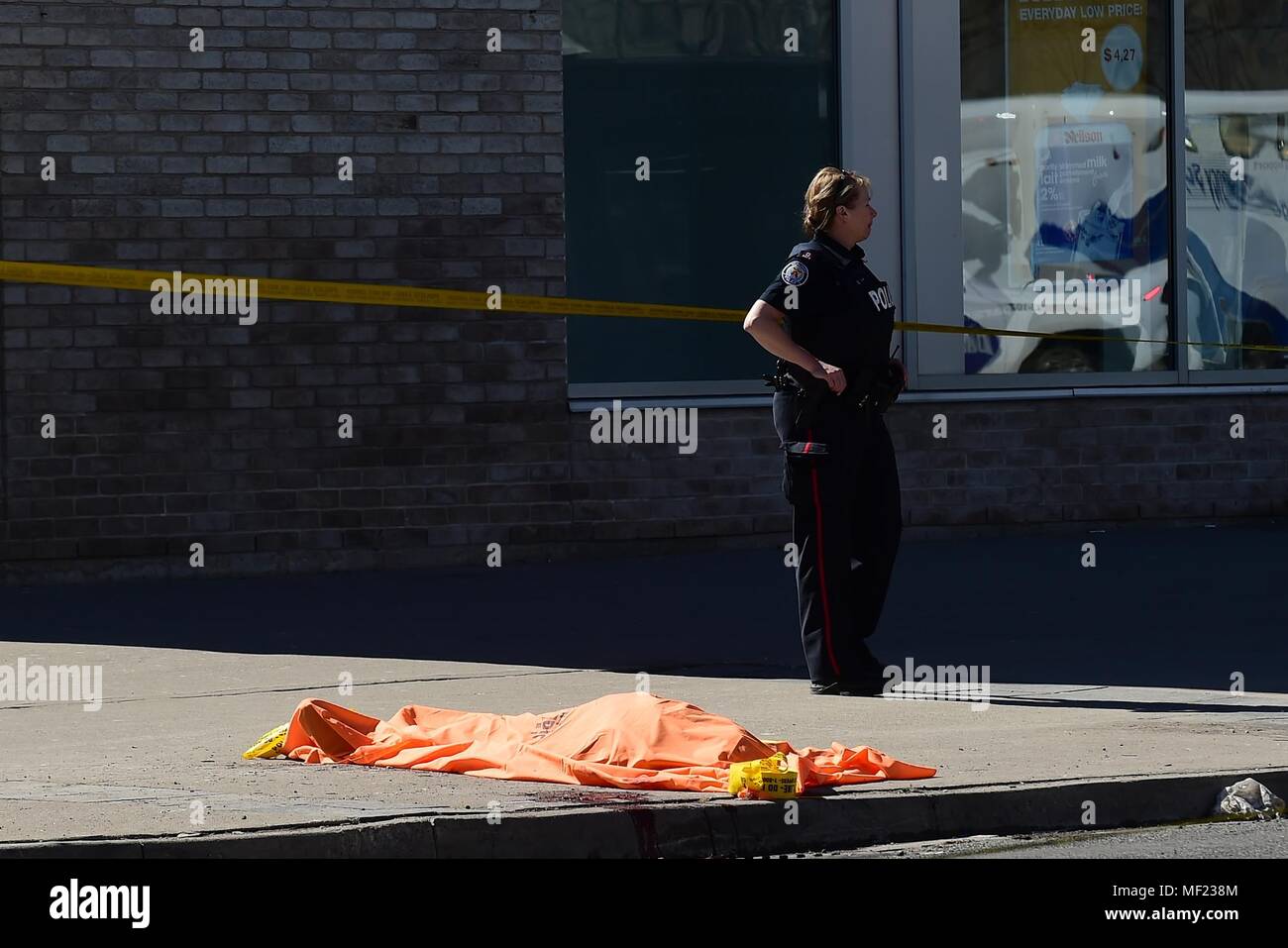 Toronto, Ontario, Canada. 23 apr, 2018. Un funzionario di polizia si erge nei pressi di un corpo coperto di Toronto dopo un van montato un marciapiede di schiantarsi in un certo numero di pedoni il lunedì. Nove persone sono state uccise e almeno 16 altri feriti dopo un camioncino bianco entra in collisione con i pedoni a Yonge e Finch a nord del centro cittadino. Hanno detto le autorità il van è stata trovata e il conducente era in stato di custodia cautelare. Credito: Victor Biro/ZUMA filo/Alamy Live News Foto Stock