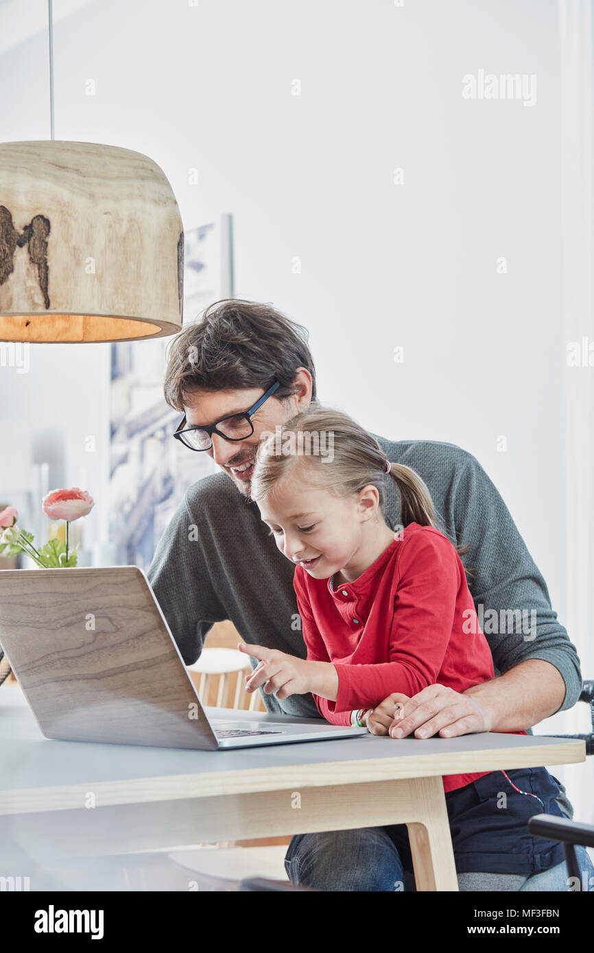 Sorridente padre e figlia utilizzando computer portatile sul tavolo a casa Foto Stock