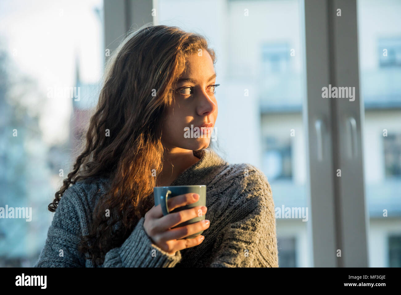 Ritratto di ragazza adolescente con tazza da caffè guardando fuori della finestra di sera Foto Stock