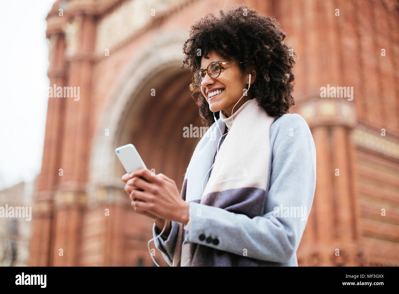 Spagna, Barcellona, donna felice con un telefono cellulare e le cuffie a una porta Foto Stock