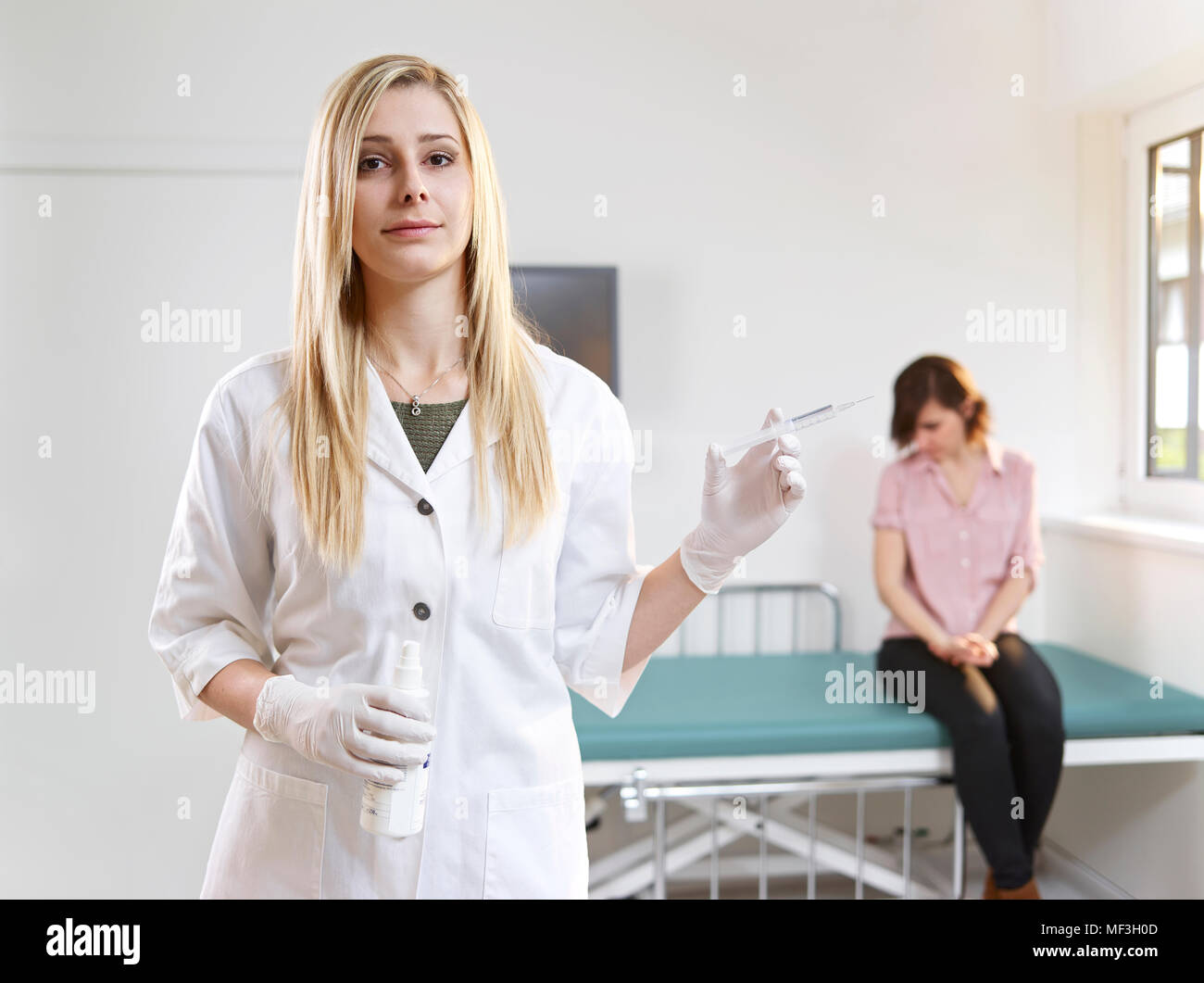 Medico donna con la siringa nella pratica medica e il paziente in background Foto Stock