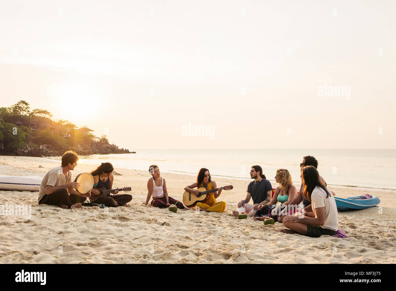 Thailandia Koh Phangan, gruppo di persone sedute su una spiaggia con la chitarra al tramonto Foto Stock