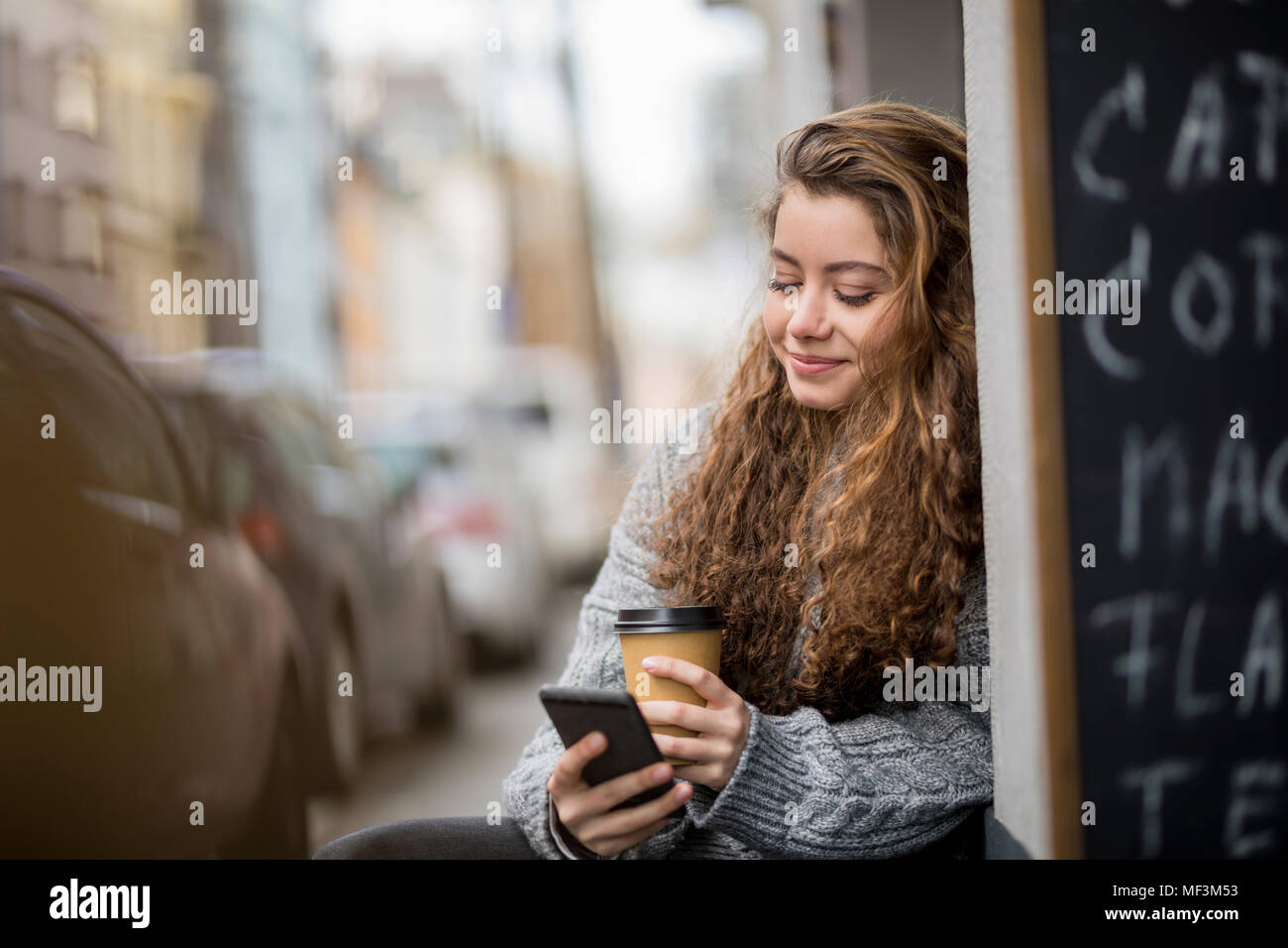 Ragazza adolescente di bere il caffè, la lettura di messaggi di testo Foto Stock