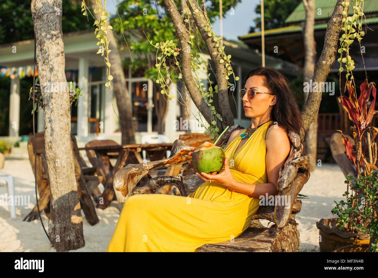 Thailandia Koh Phangan, donna seduta in un caffè sulla spiaggia a bere acqua di cocco. Foto Stock