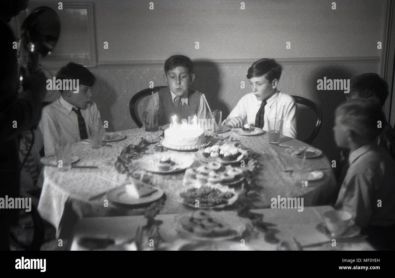 1948, storico, giovane ragazzo soffiando fuori le candeline sulla sua torta di compleanno come egli ha un compleanno tea party con i suoi amici Foto Stock