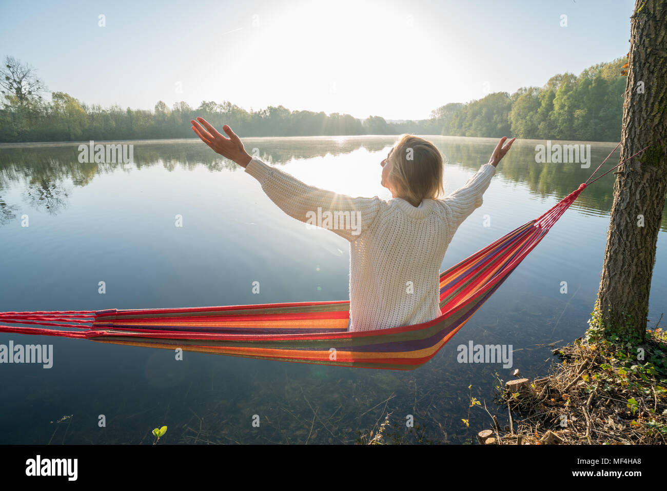 Giovane donna su amaca in riva al lago che abbraccia la natura con le braccia spalancate, persone viaggi riuscita realizzazione del concetto. Francia, Europa Foto Stock