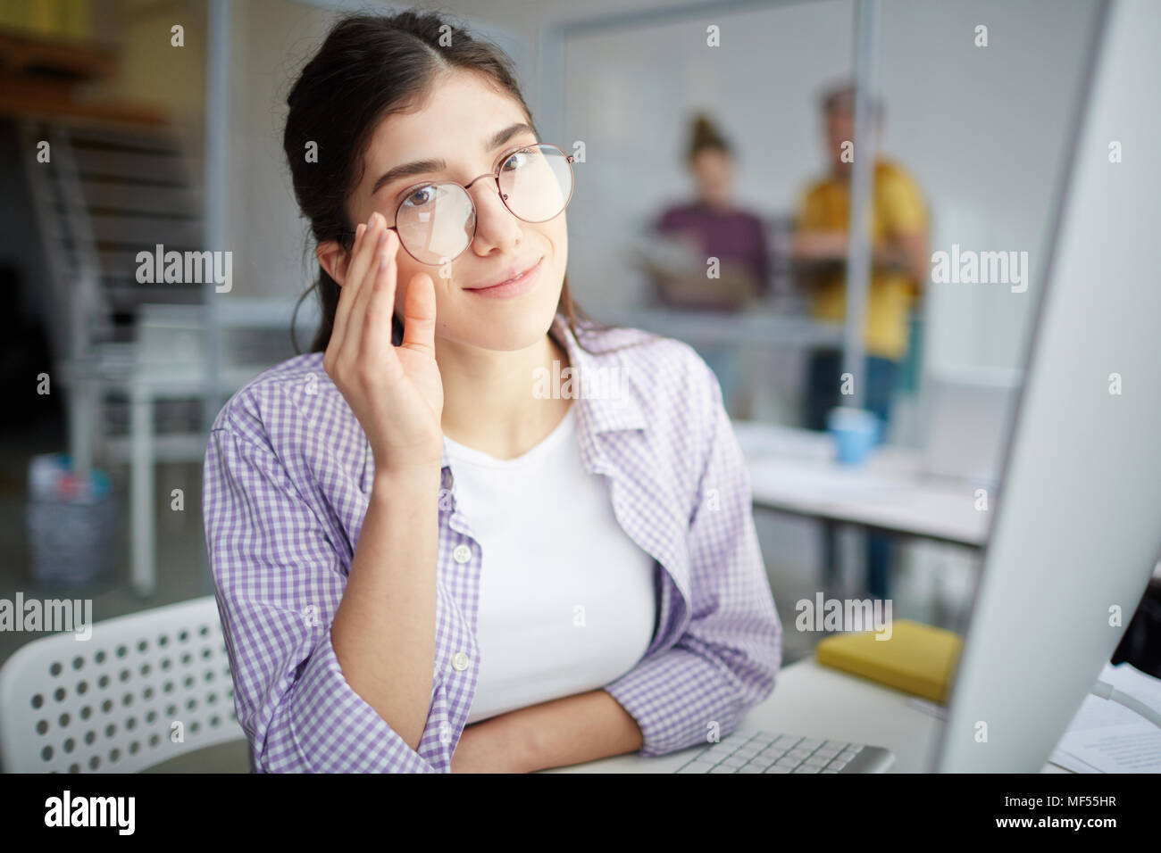 Ritratto di giovane lavoratore informale in occhiali seduto in ufficio Foto Stock